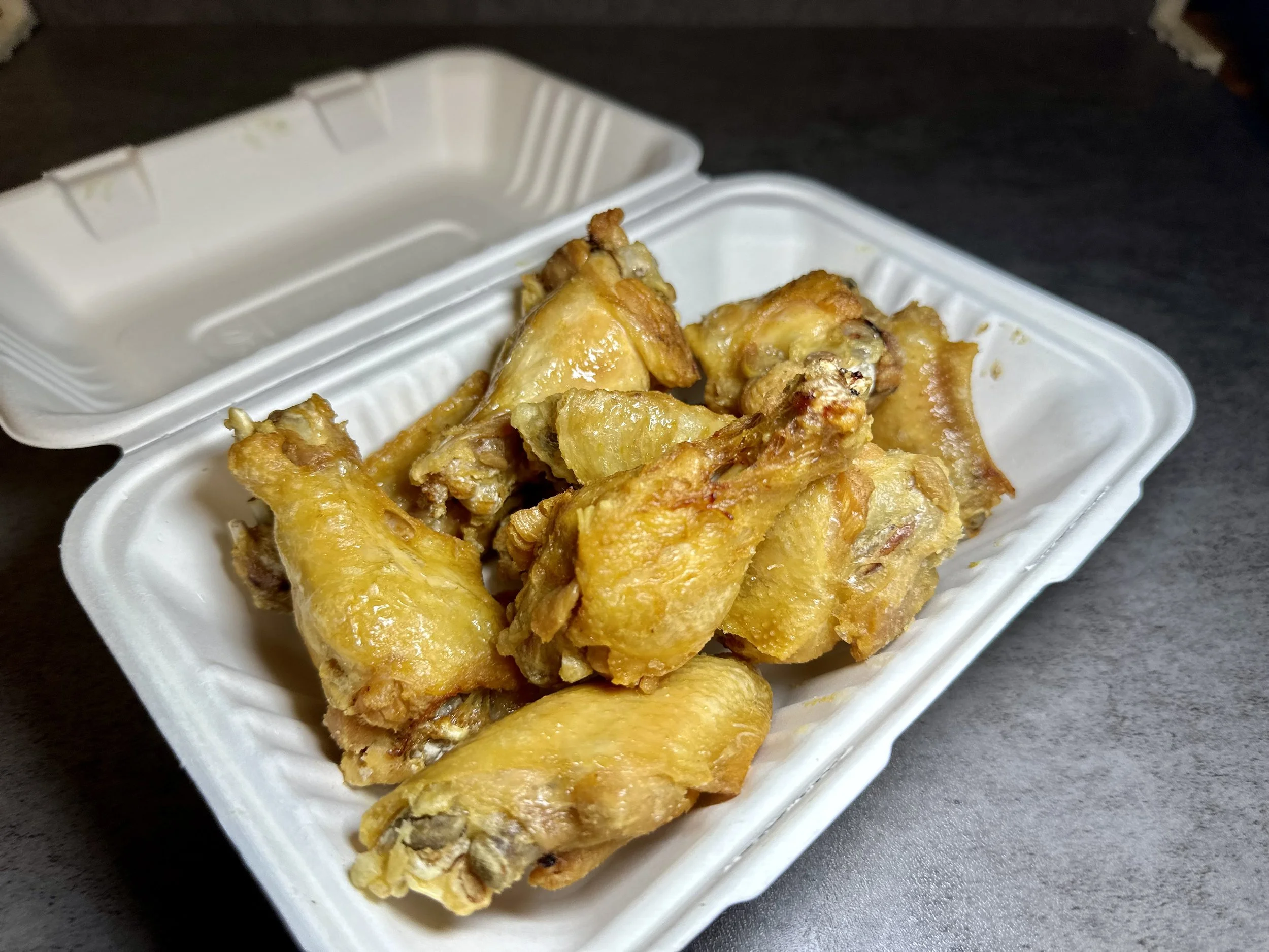 Fried chicken wings in a white takeout container placed on a dark surface.