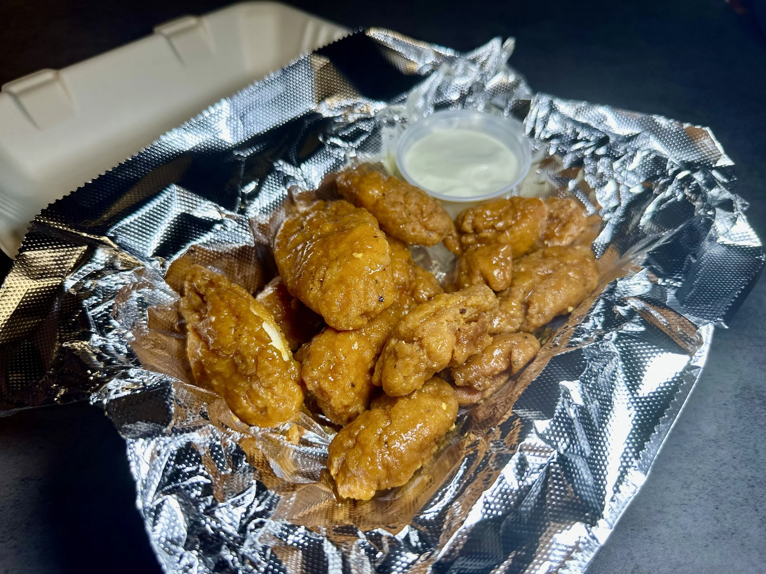 Fried chicken pieces with dipping sauce in a foil-lined container