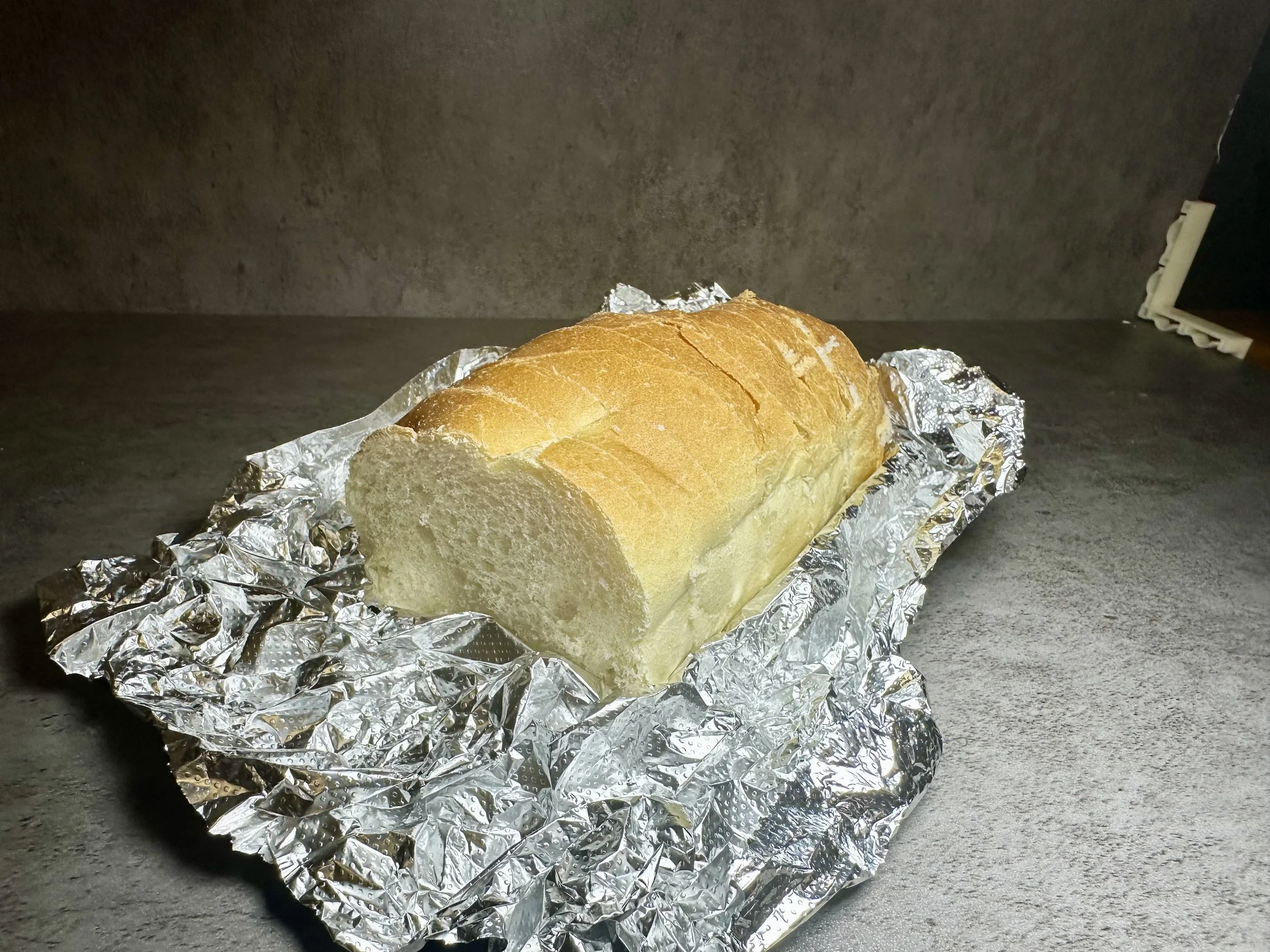 A loaf of bread on crinkled aluminum foil on a dark gray surface with a gray background.