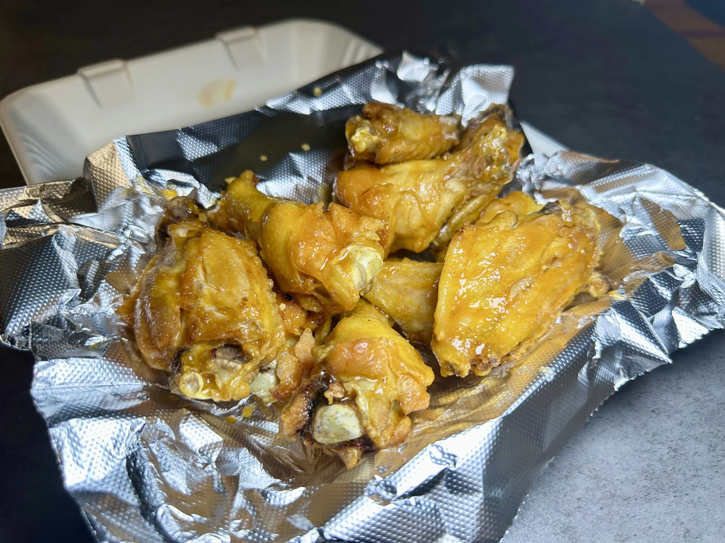 Cooked chicken wings on aluminum foil in a paper food tray, served on a dark surface.