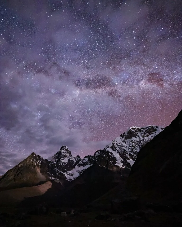 Night sky filled with stars above snow-capped mountain peaks.