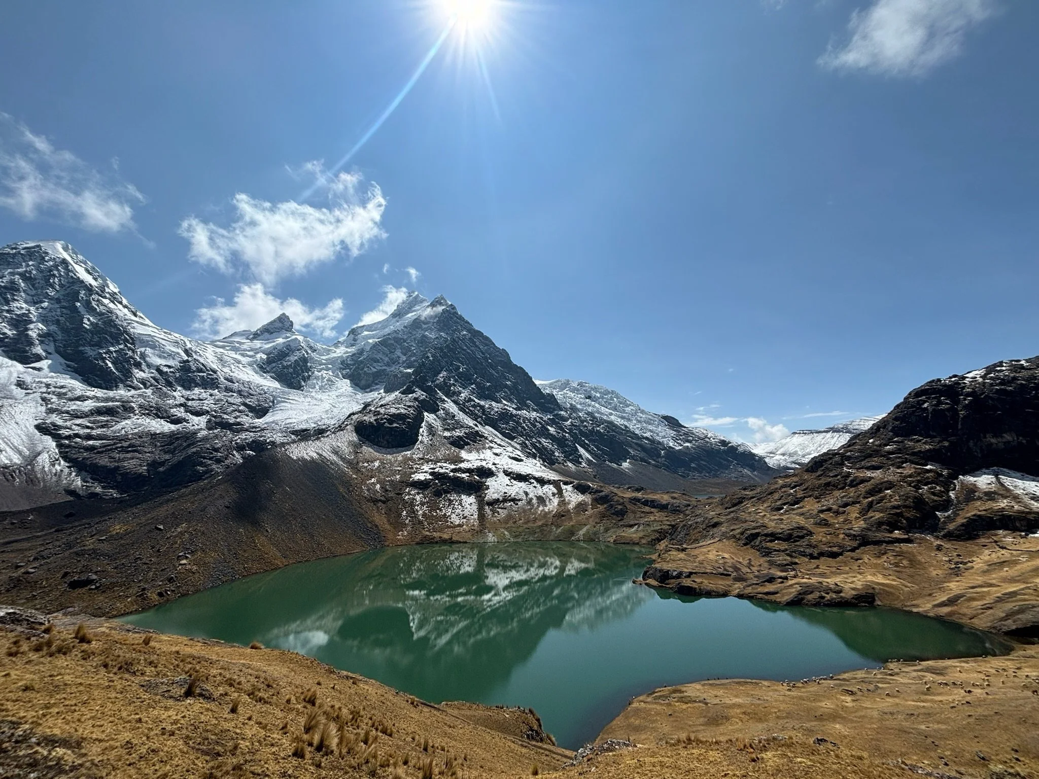 Snow-capped mountains and a small green lake in a mountainous landscape on a clear, sunny day with a blue sky.