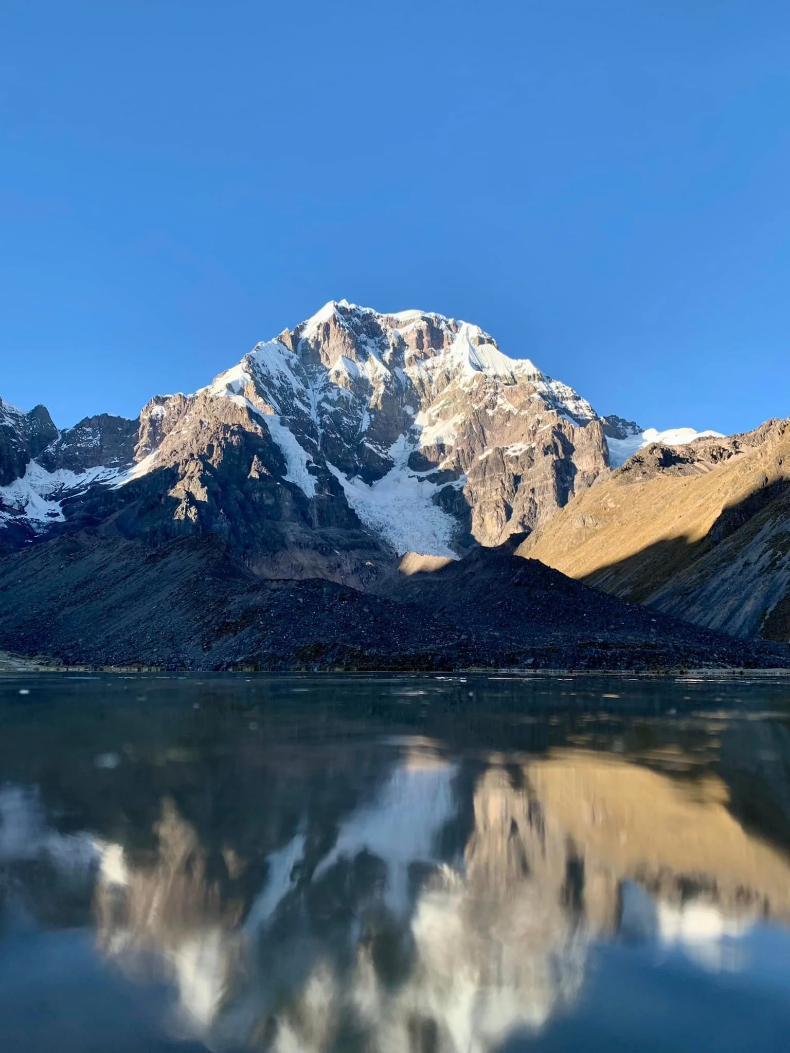 Snow-capped mountain reflected on a calm lake under a clear blue sky.