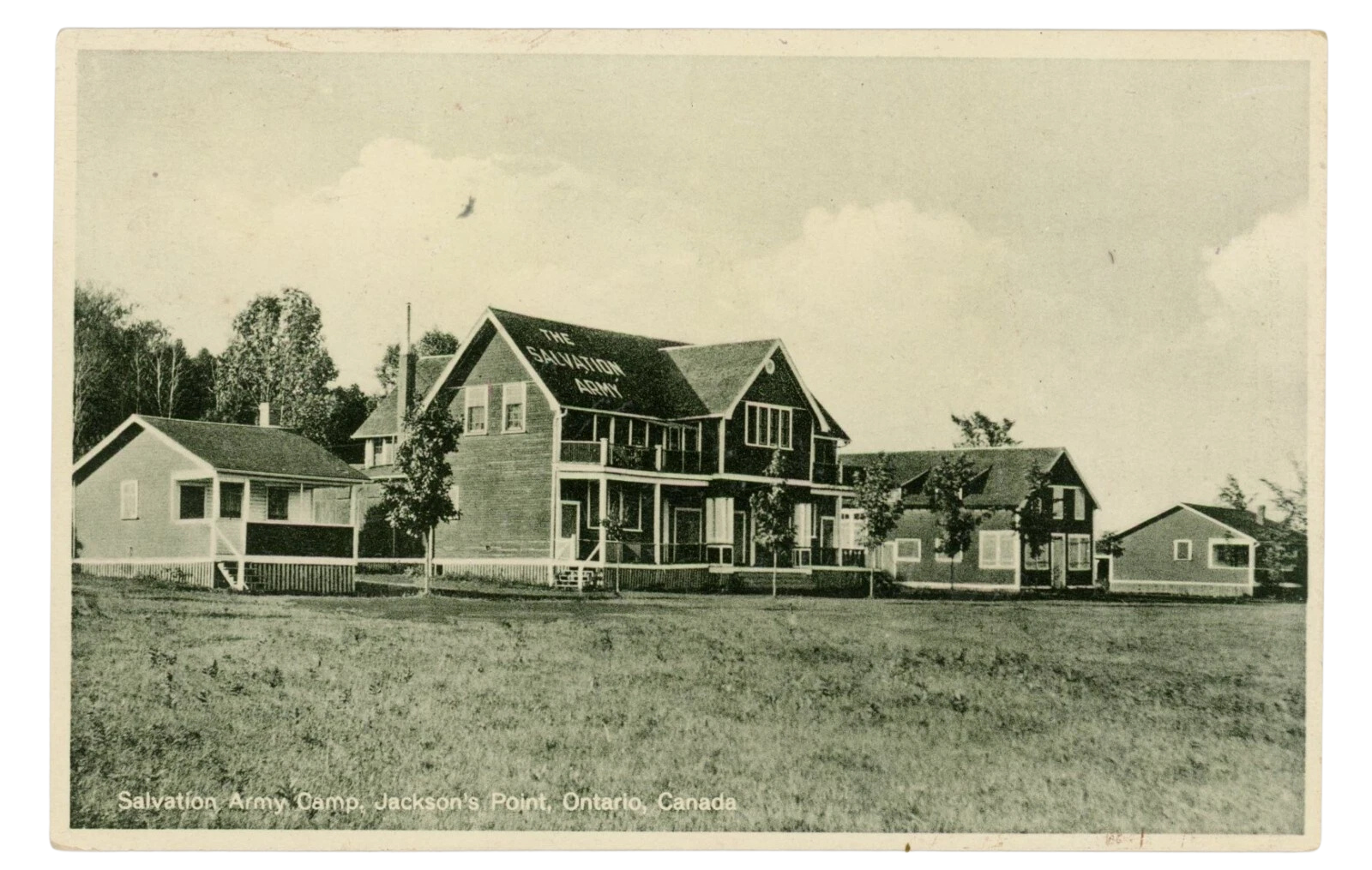 Black and white photo of Salvation Army camp buildings at Jackson's Point, Ontario, Canada, with trees and open grassy area in the foreground.