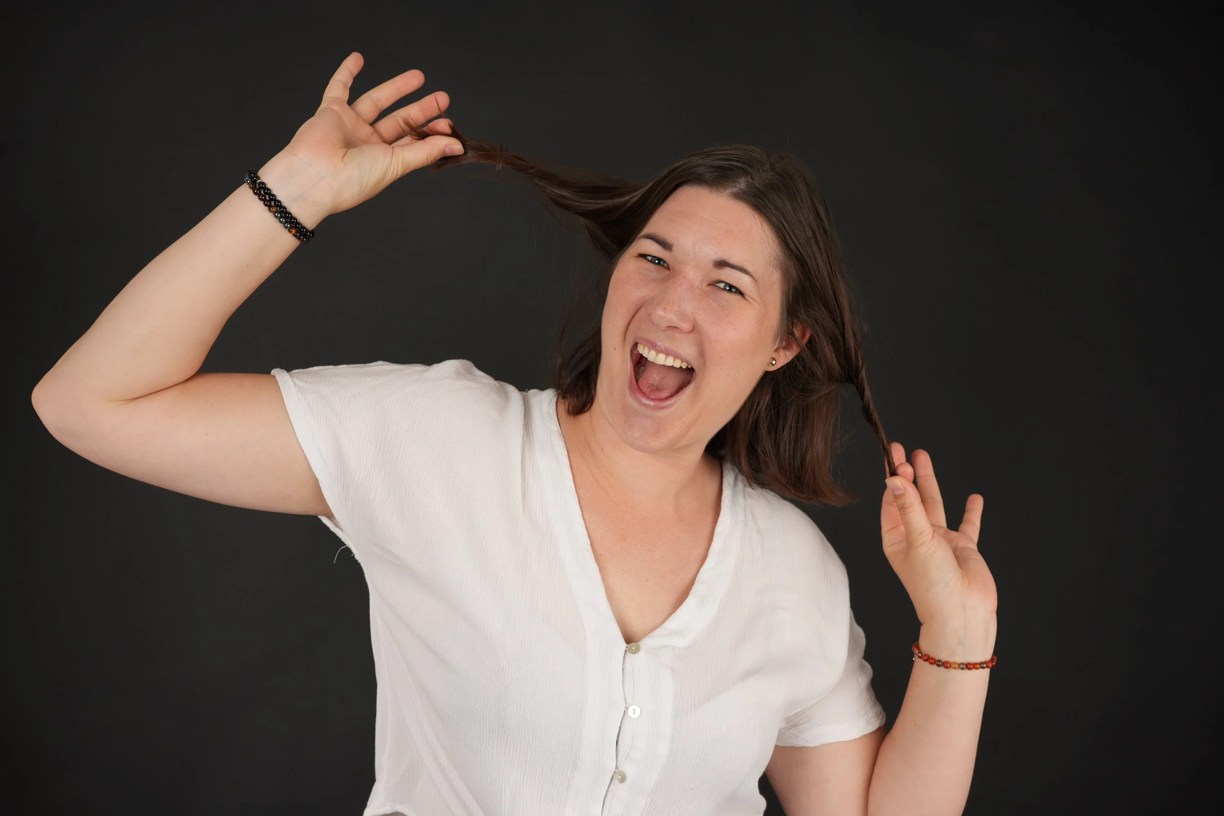 Junge Frau mit braunen Haaren und White-Shirt, lachend, spielt mit ihren Zöpfen, schwarze Hintergrund.