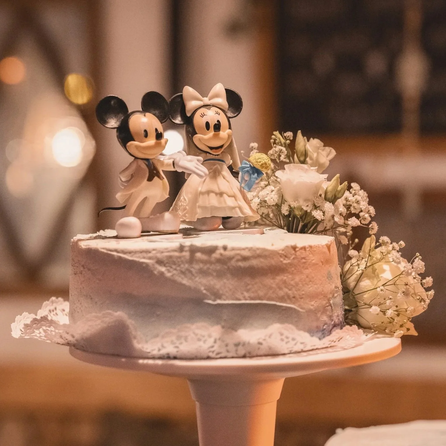 Ein Geburtstagskuchen mit Mickey und Minnie Mouse Figuren als Dekoration, umgeben von weißen Blumen.