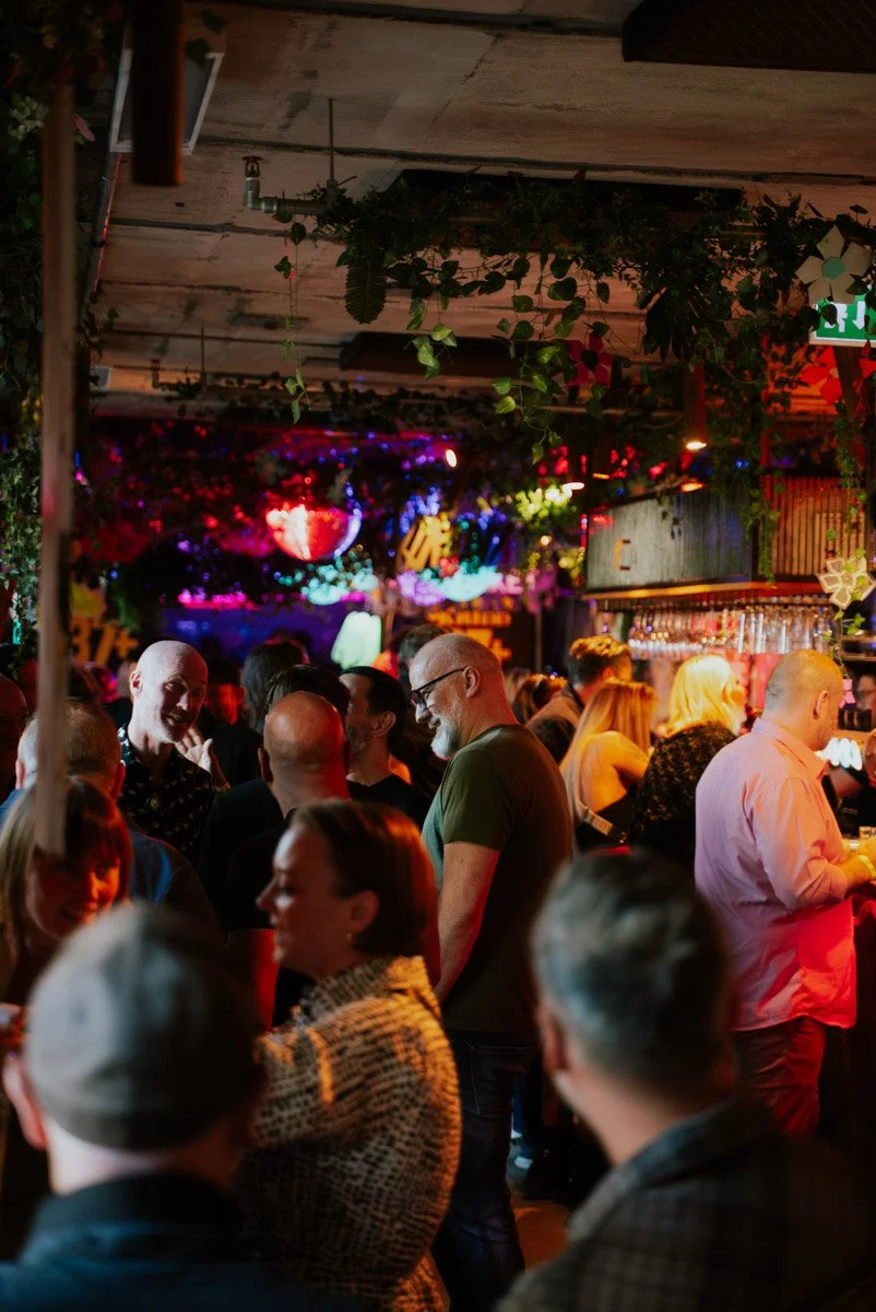 Mennesker samles i en bar med fargerik, stemningsfull belysning og dekorasjoner.