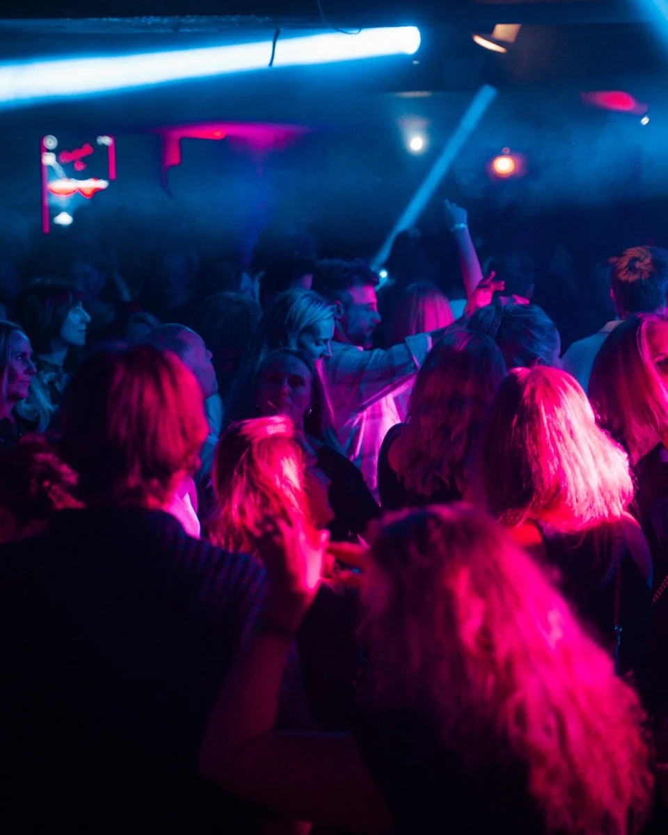 Mennesker danser og hygger seg på en nattklubb med fargerikt lys og en dansegulv.