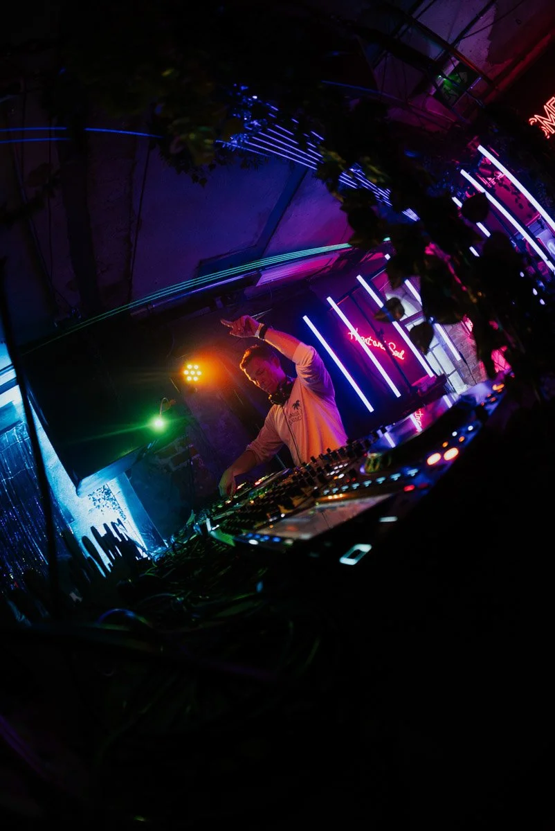 En person som DJ spiller musikk på en klubb eller konsert med fargerik belysning.