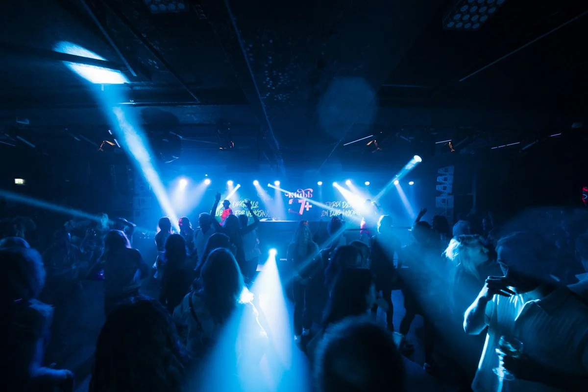 Dansende mennesker danser i en nattklubb med blå lys og diskokuleffekt.