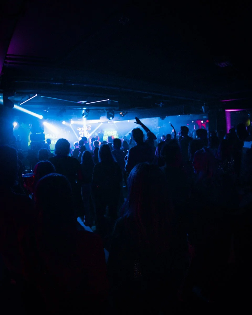 En gruppe mennesker danser og hygger seg på en klubb med mørk belysning og fargede lys.