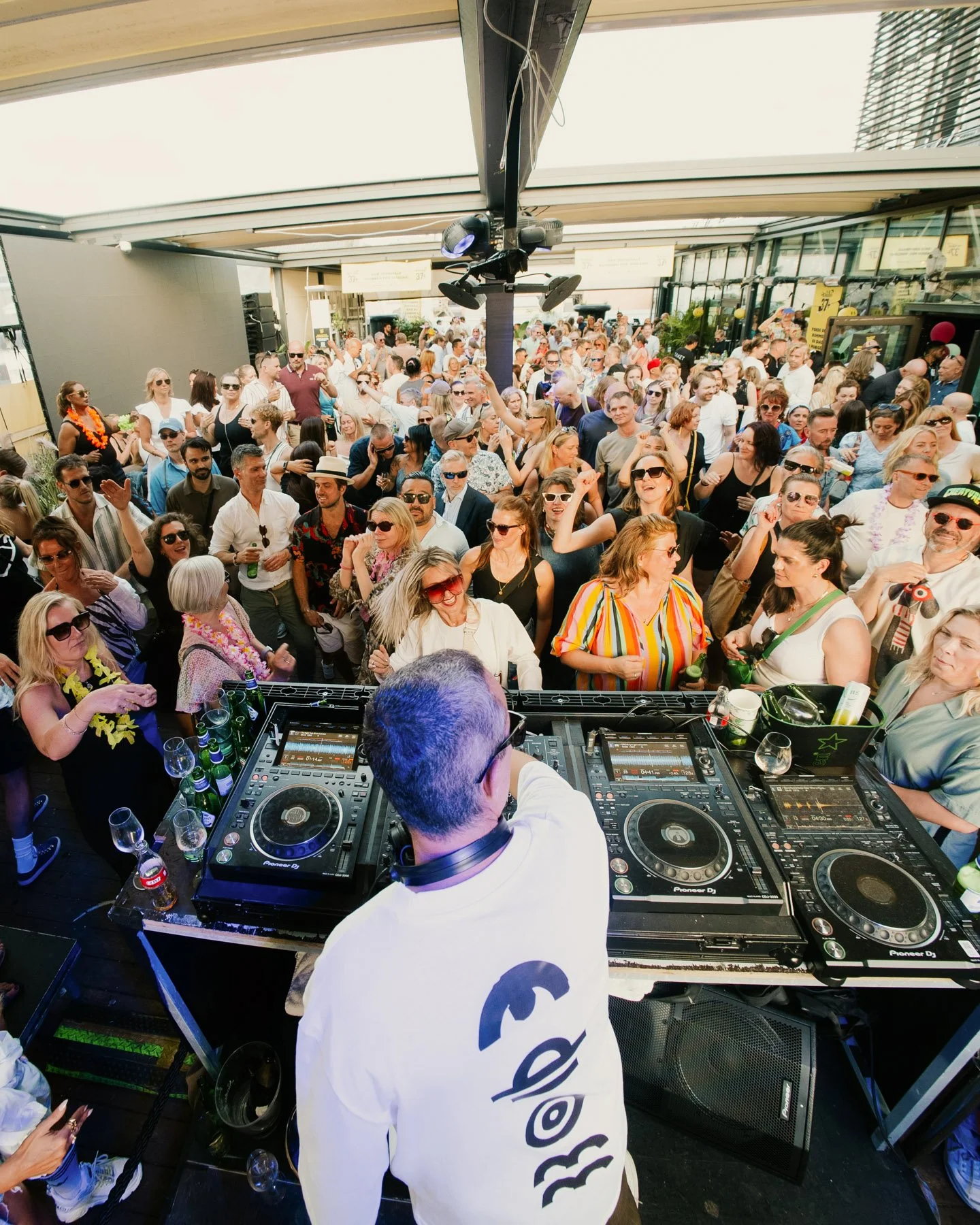 En DJ spiller på en plattform foran en stor folkemengde under en utendørs festival eller klubbarrangement.