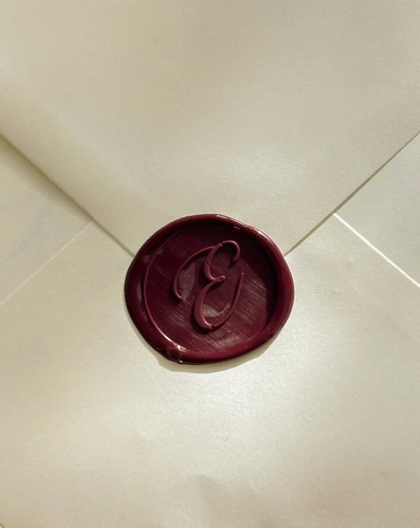 A red wax seal with an embossed letter 'C' on white tiled surface.