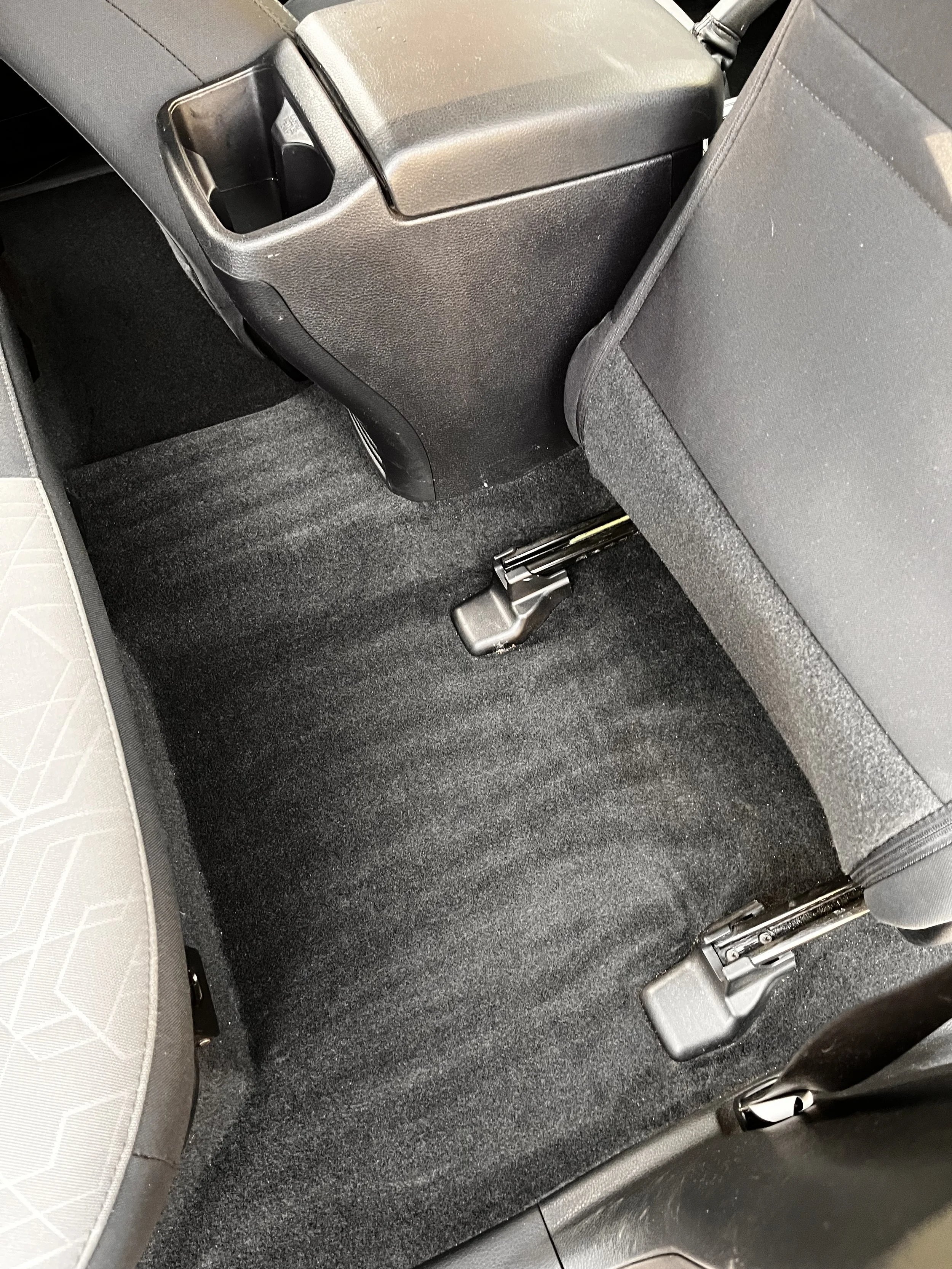 Backseat floor area of a car, showing black carpeted flooring and the rear seat mounting points.
