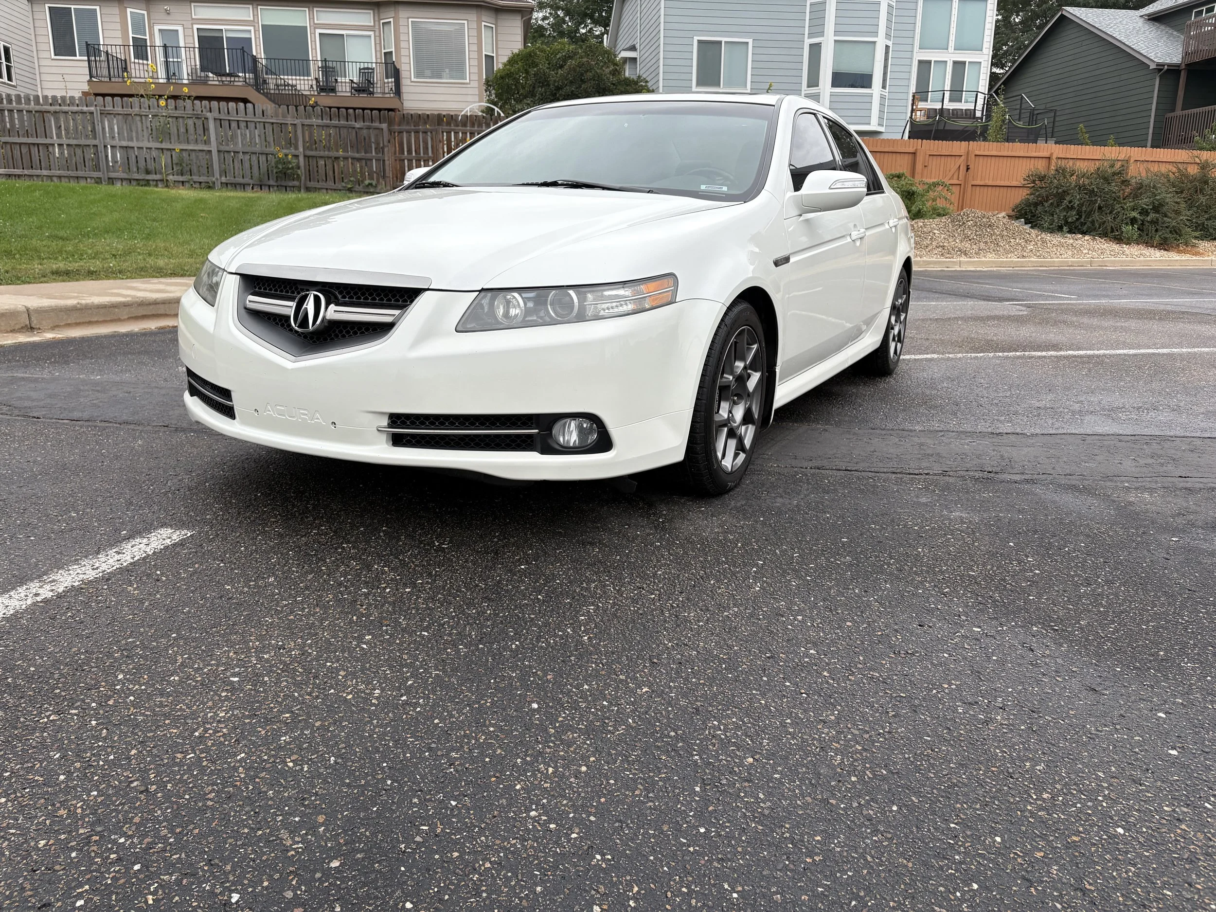 White Acura sedan parked in a parking lot with residential buildings in the background.