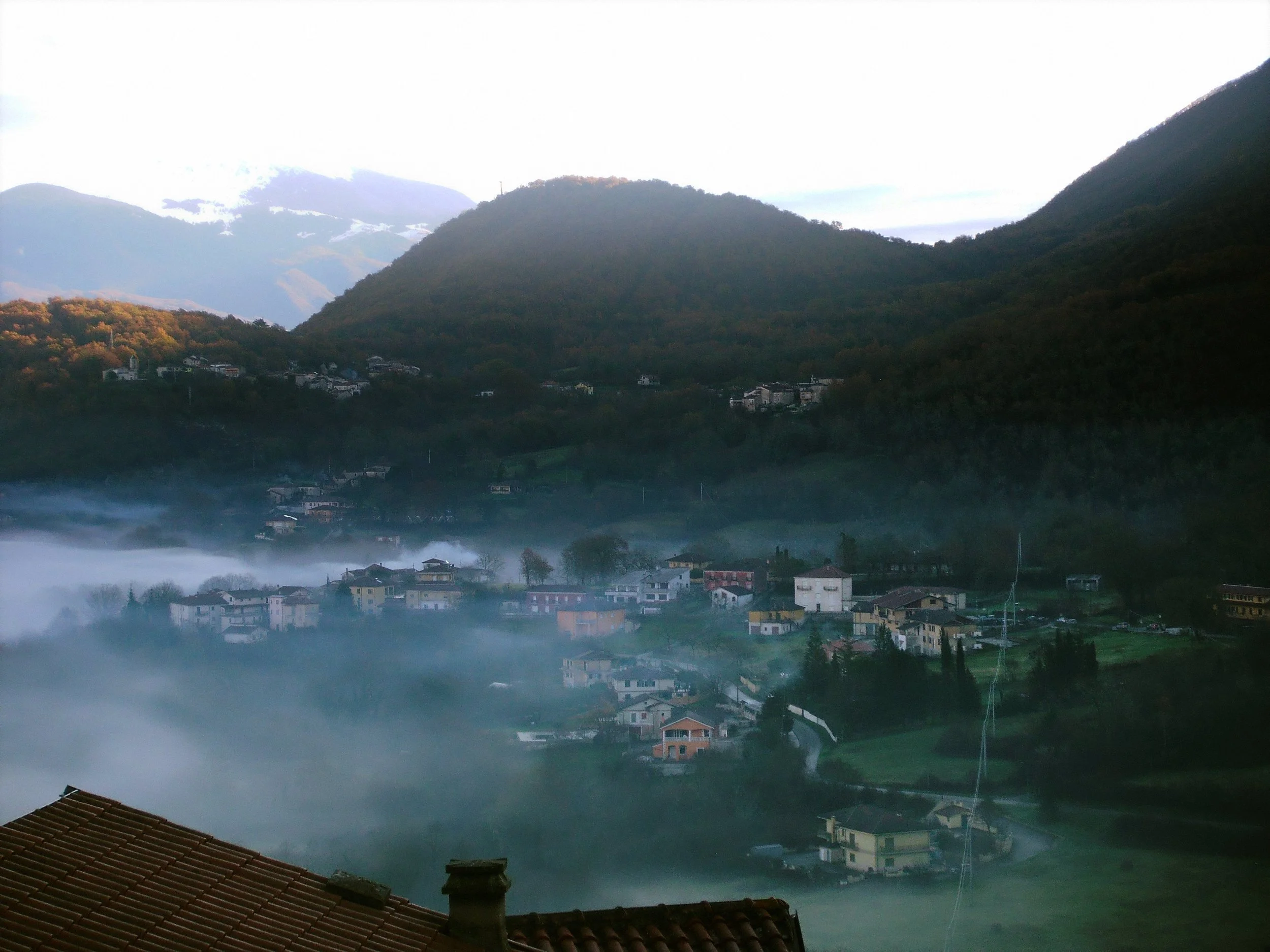 Mountains surrounding a foggy valley with houses and trees in a rural landscape.