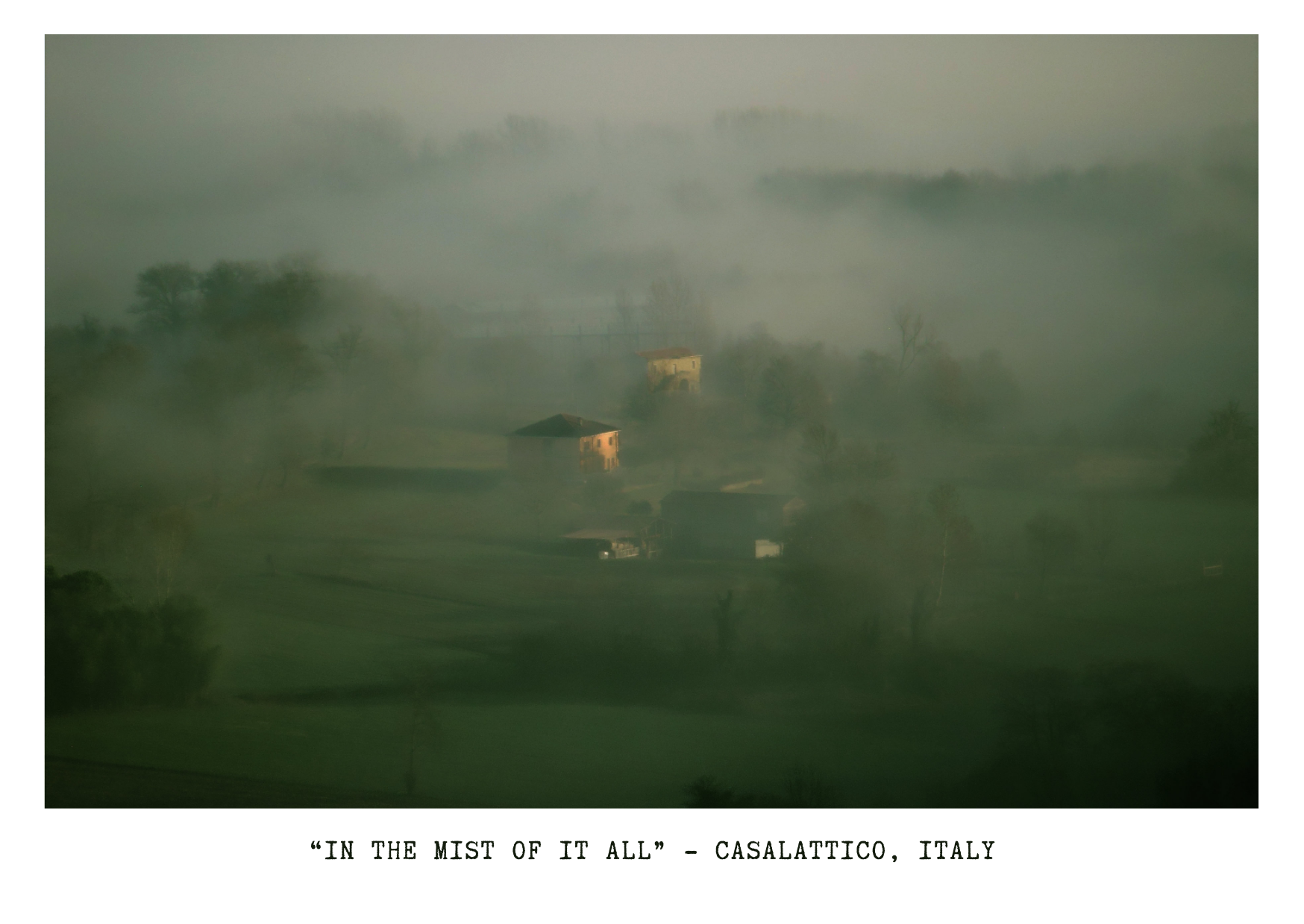 A misty landscape in Casalaticco, Italy, featuring several houses and trees partially obscured by fog.