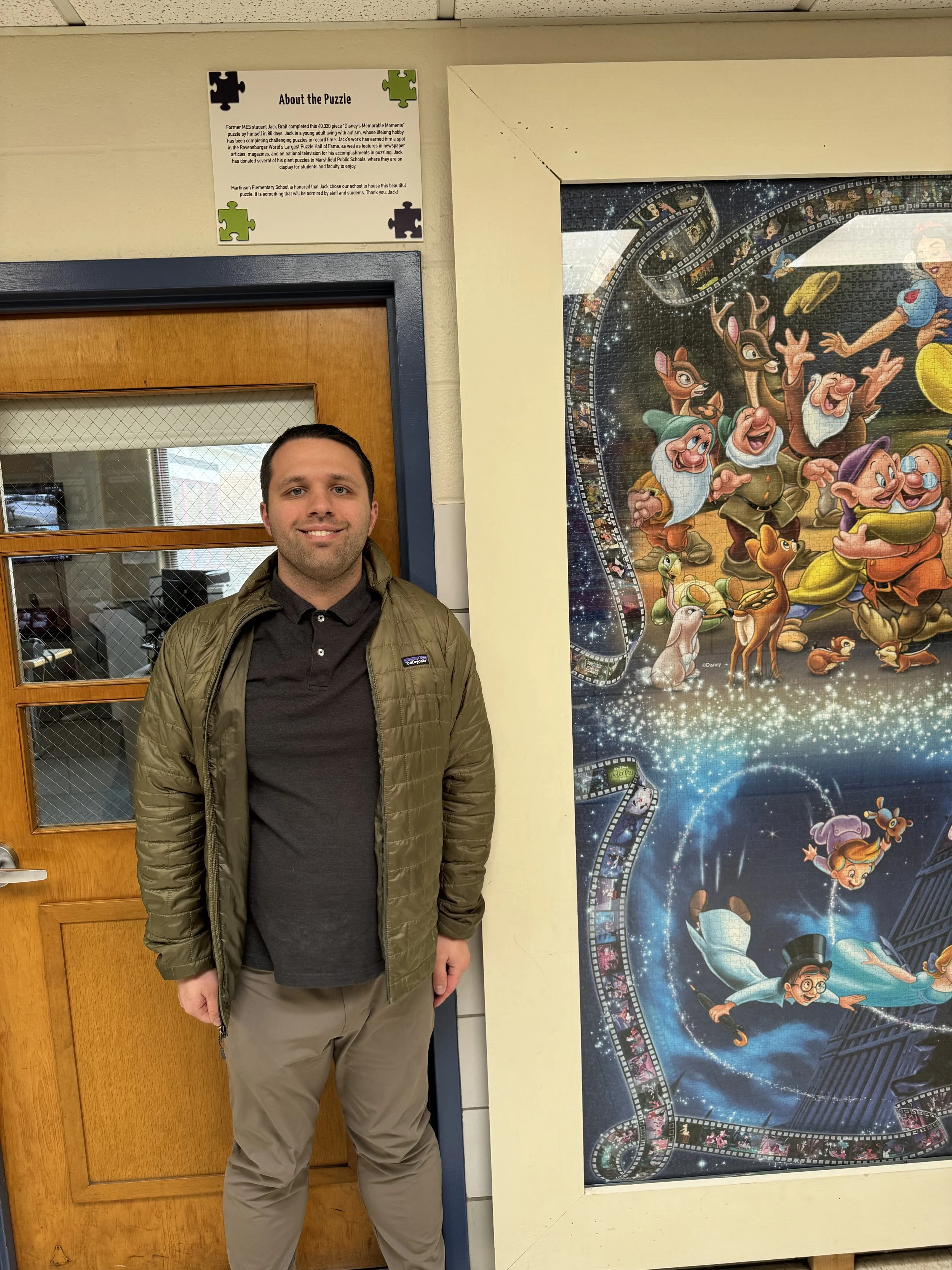 Jack Brait, aka Jack Of Puzzles, under the plaque of the 40,320 piece Disney puzzle at Martinson Elementary School in Marshfield, MA