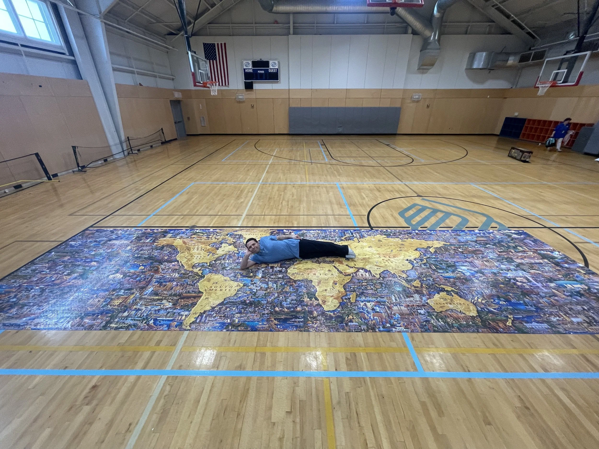 Jack Brait, aka Jack Of Puzzles, lying on the  60,000 piece puzzle at the gymnasium at the Boys and Girls Club of Marshfield, MA. The puzzle was made from Dowdle Folk Art (Dowdle Puzzles) the work’s largest puzzle