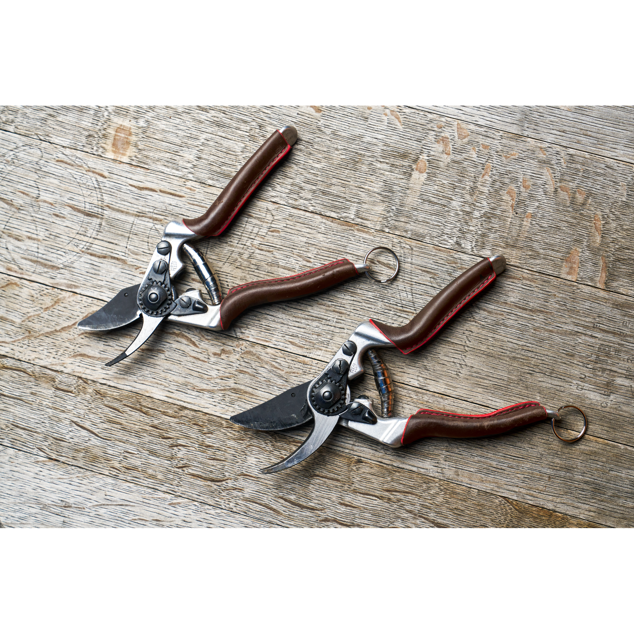 Zwei Garten-Scheren mit braunen Griffen auf einem Holztisch.