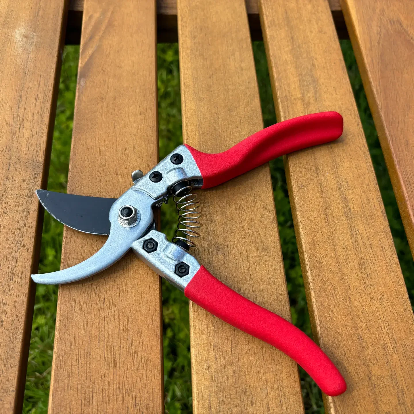 Gartenschere mit rotem Griff auf einem Holztisch.