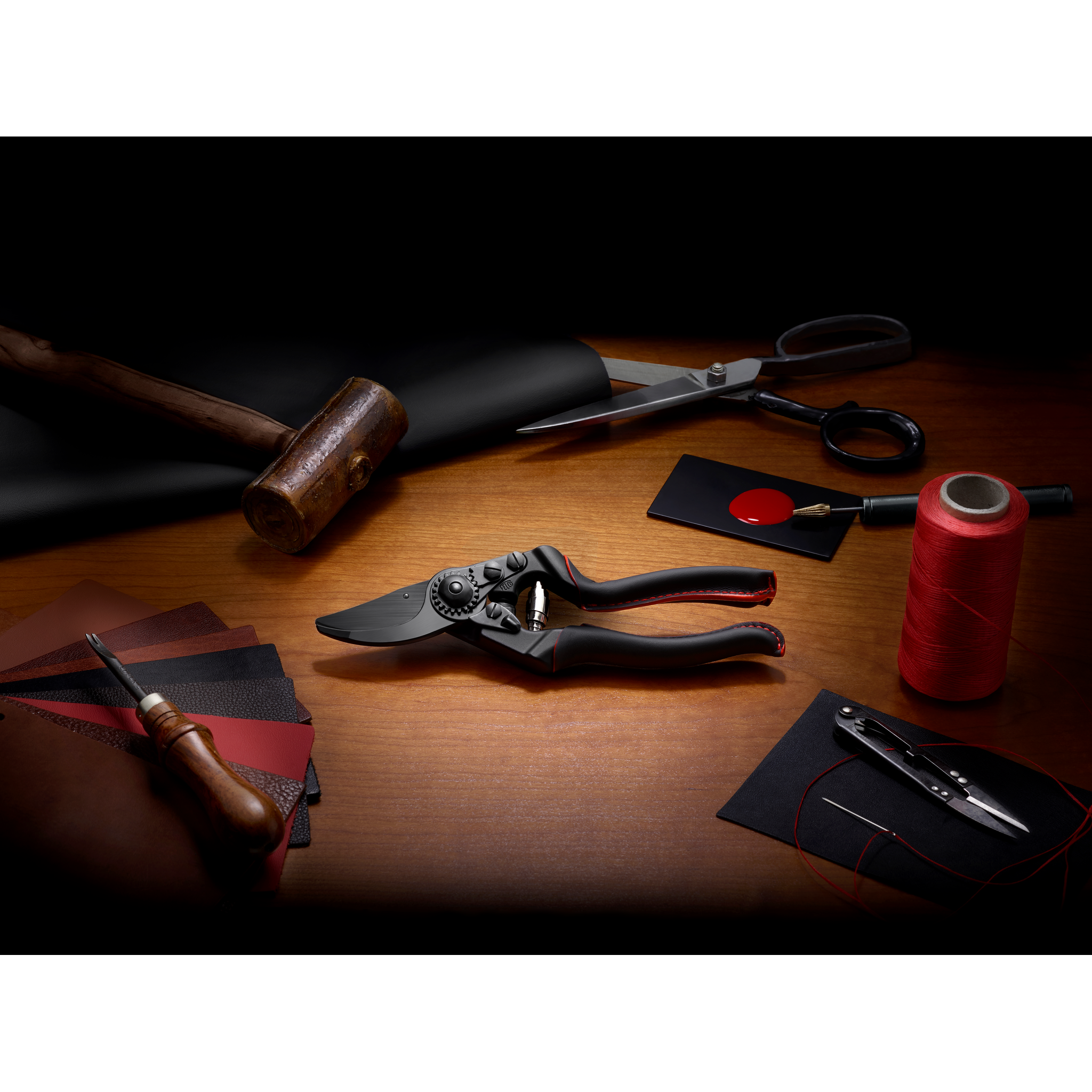 Schnittwerkzeuge, Stoffmuster, Faden, Nadel, schwarzes Lederbahn, Hammer, Schere, Handstanze auf Holztisch