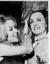 Two women, one wearing a crown, smiling and interacting with each other in a black and white photo.