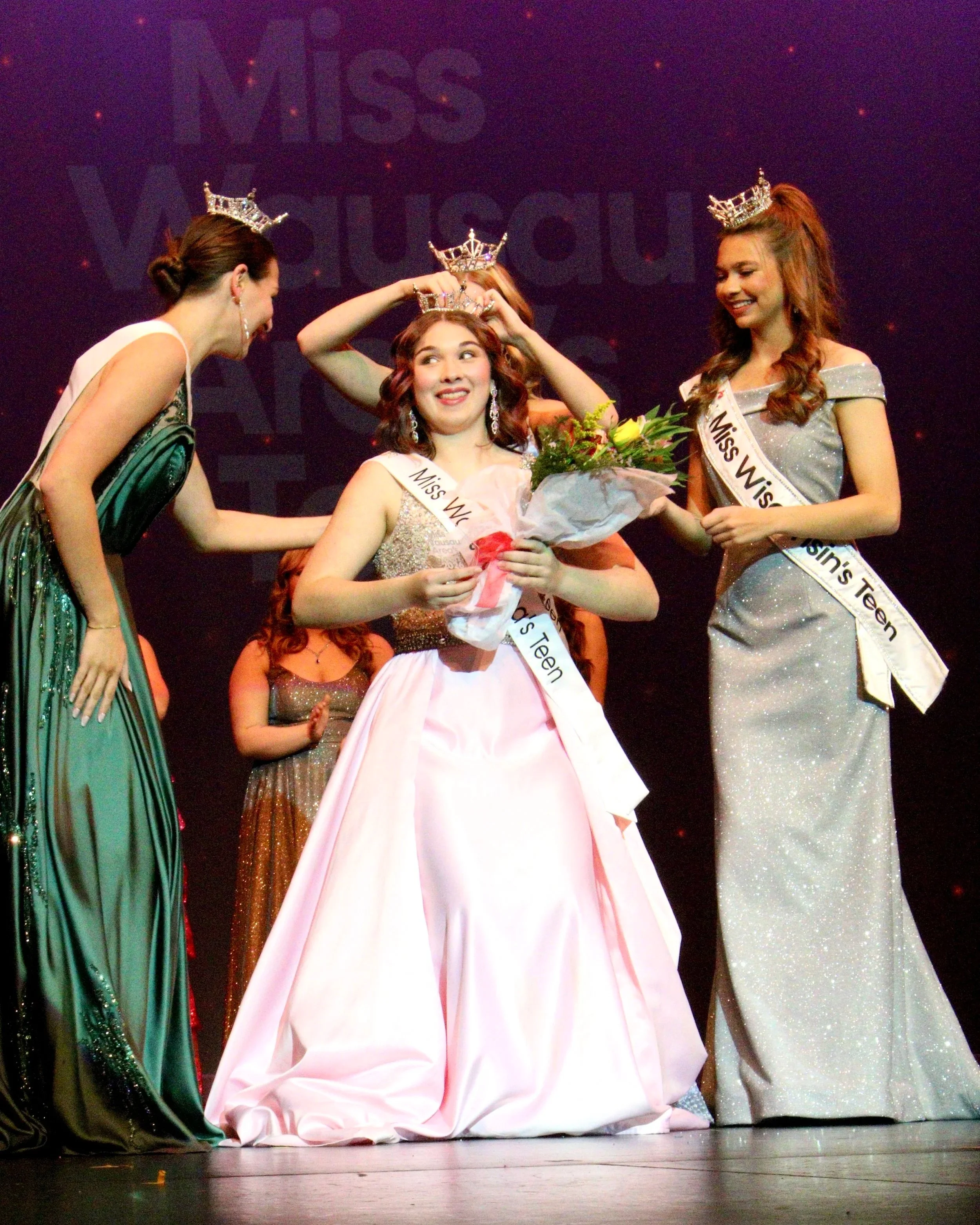 Miss Wausau Area's Teen 2026 crowned with Miss Wisconsin's Teen during a pageant, with other contestants congratulating her on stage. Chloe Munguia.