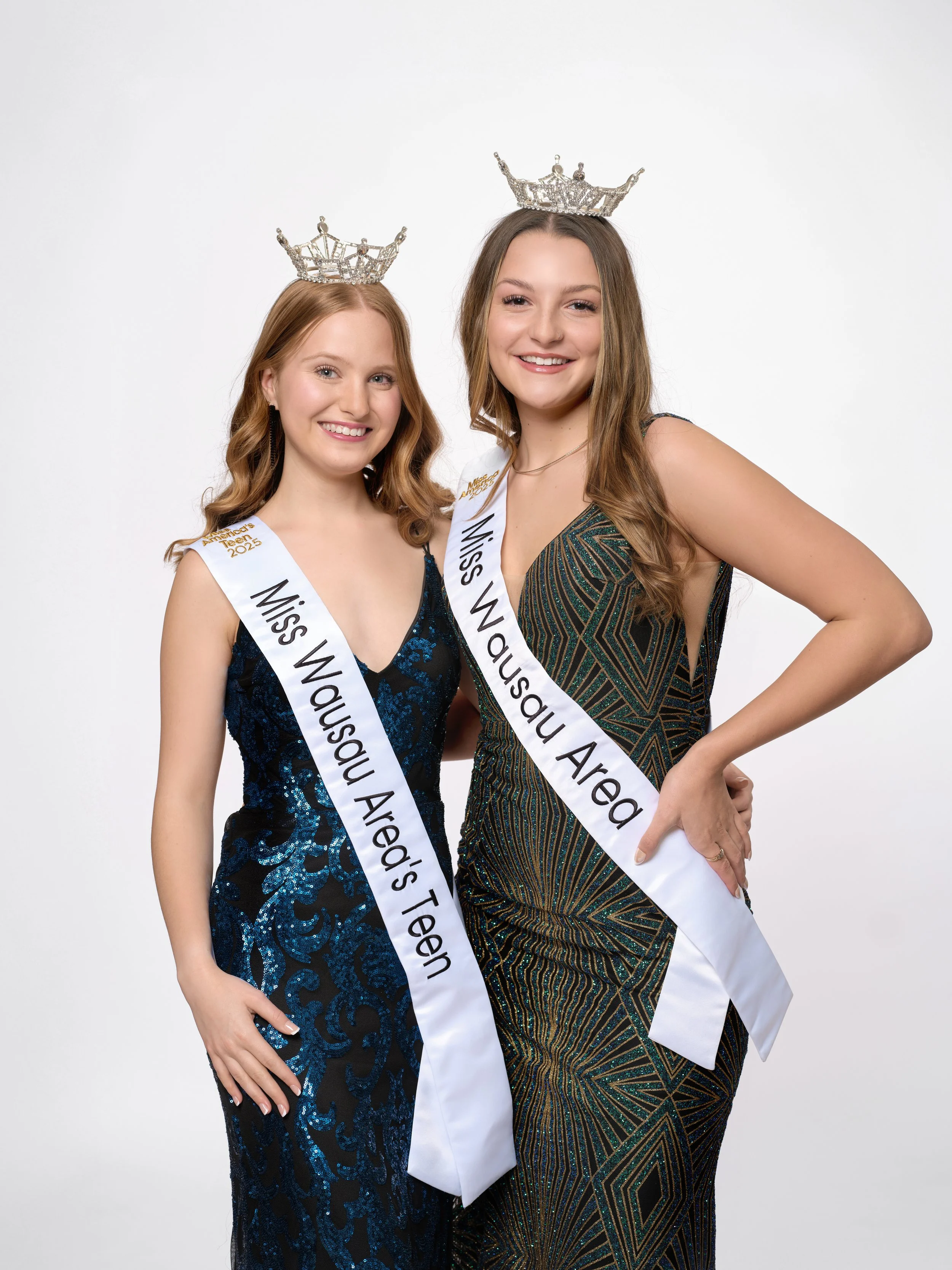Two young women wearing crowns and sashes that read 'Miss Wausau Area Teen' and 'Miss Wausau Area's Teen' pose together against a white background, smiling. Avery Manthe and Anna Jacobson.
