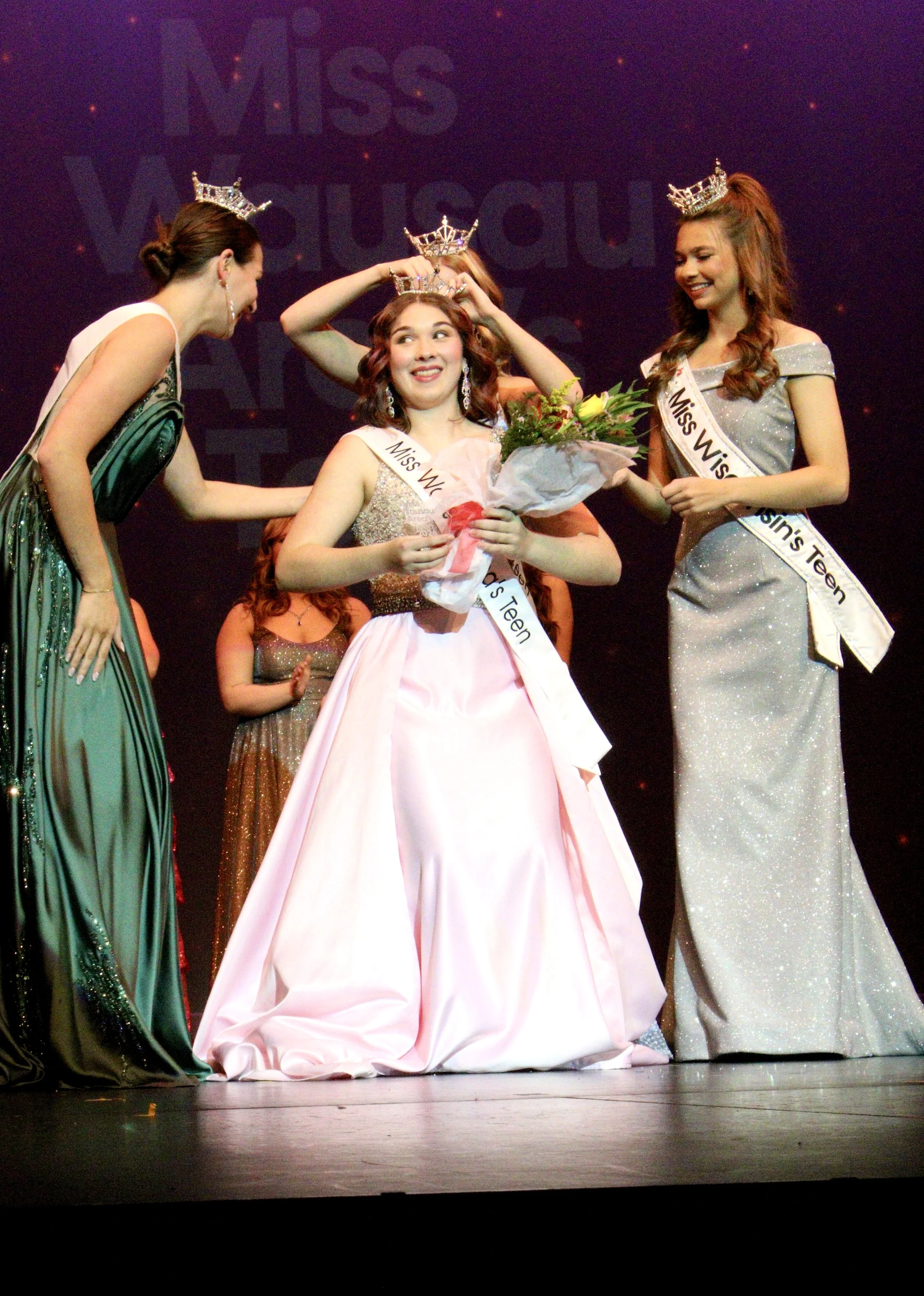Miss Wausau Area's Teen, Chloe Munguia, being crowned at a beauty pageant, holding a bouquet of flowers, with other contestants on stage.