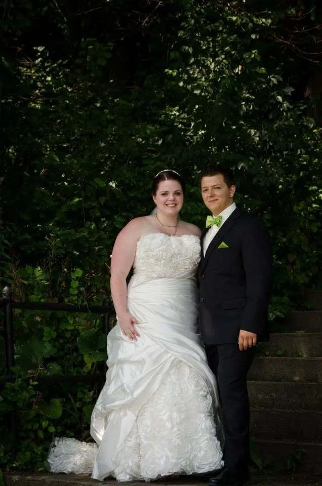 Ashley and her husband in a formal wedding portrait surrounded by greenery