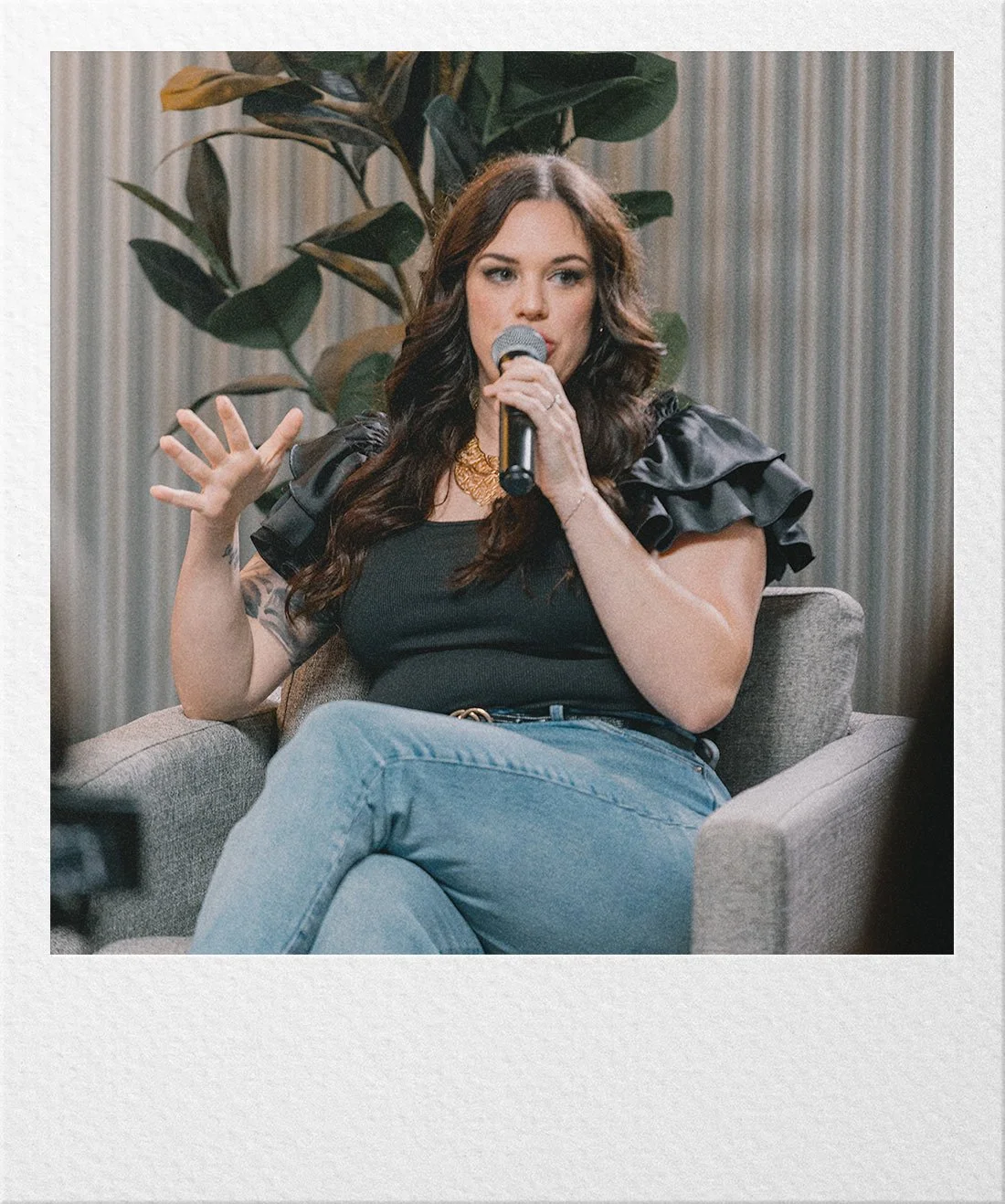 Ariel seated on a chair with a microphone speaking on a panel.