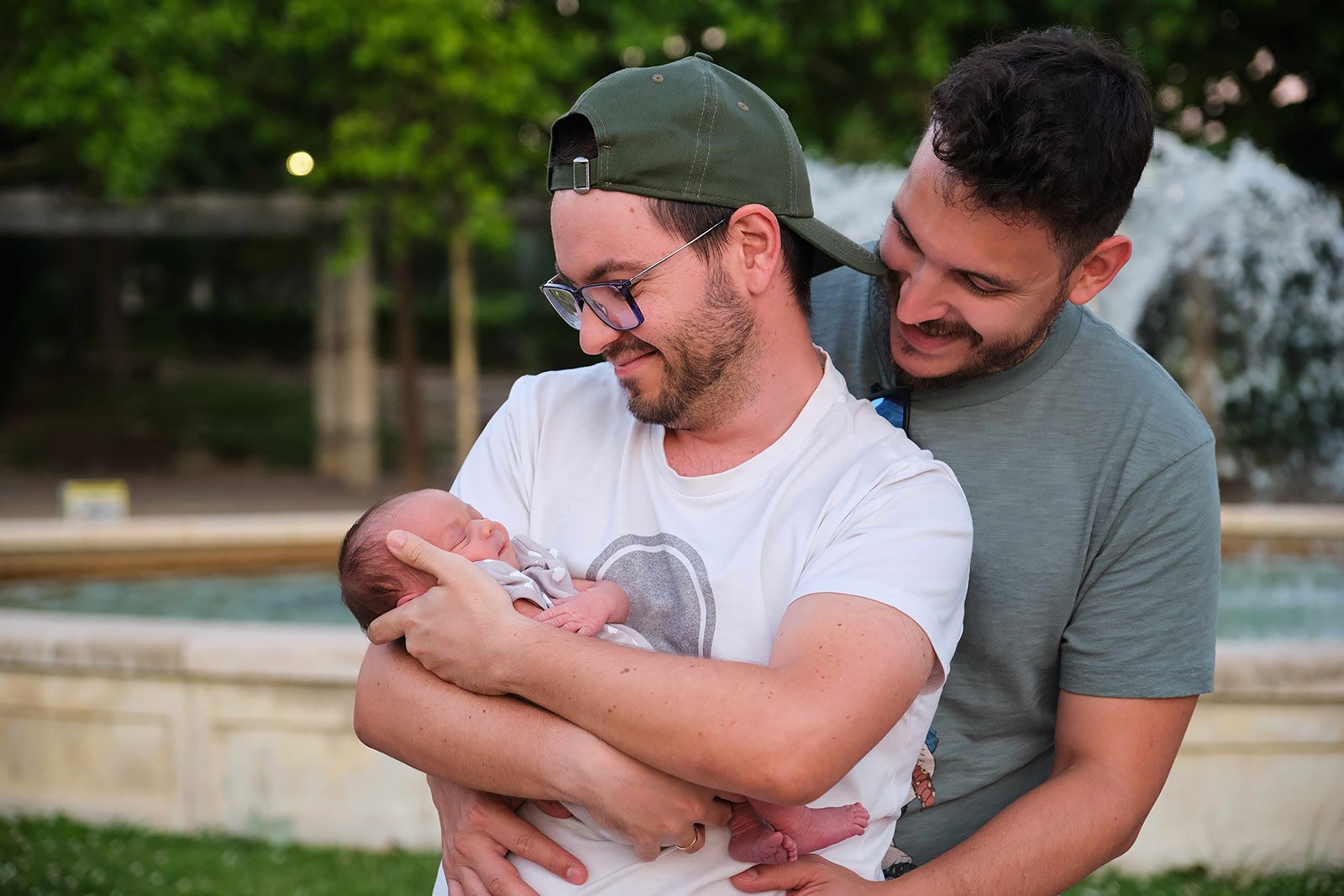 Two parents holding a newborn baby together outdoors.