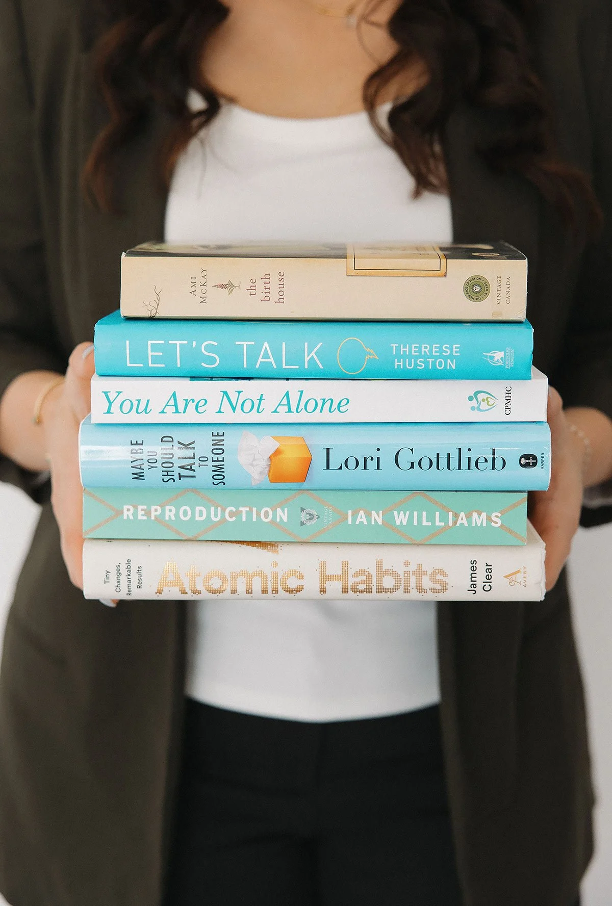 A person holding a stack of books related to mental health and personal growth.