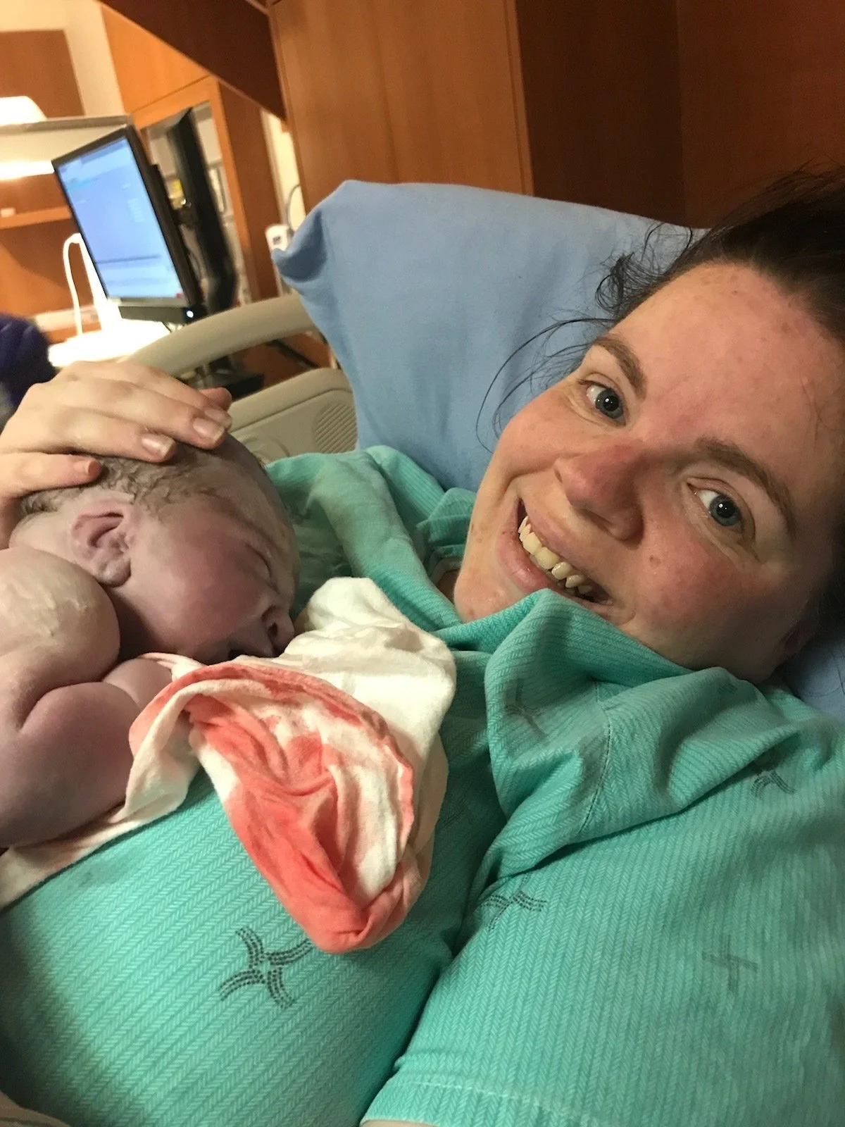 Ashley smiling and holding her newborn skin-to-skin in the hospital