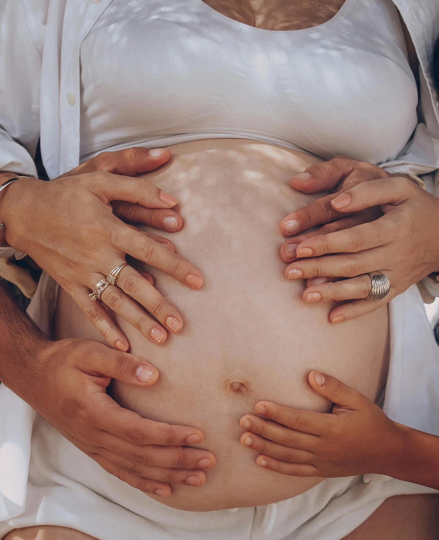 Multiple hands resting on a pregnant belly, representing collaborative support in a surrogacy journey.