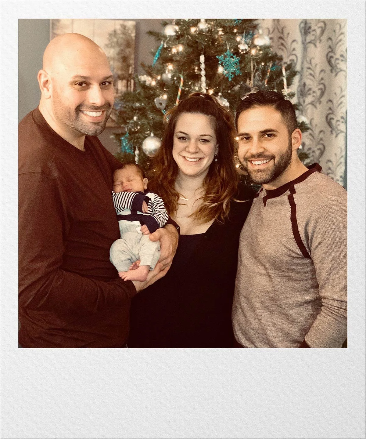 A family standing together indoors holding a baby.