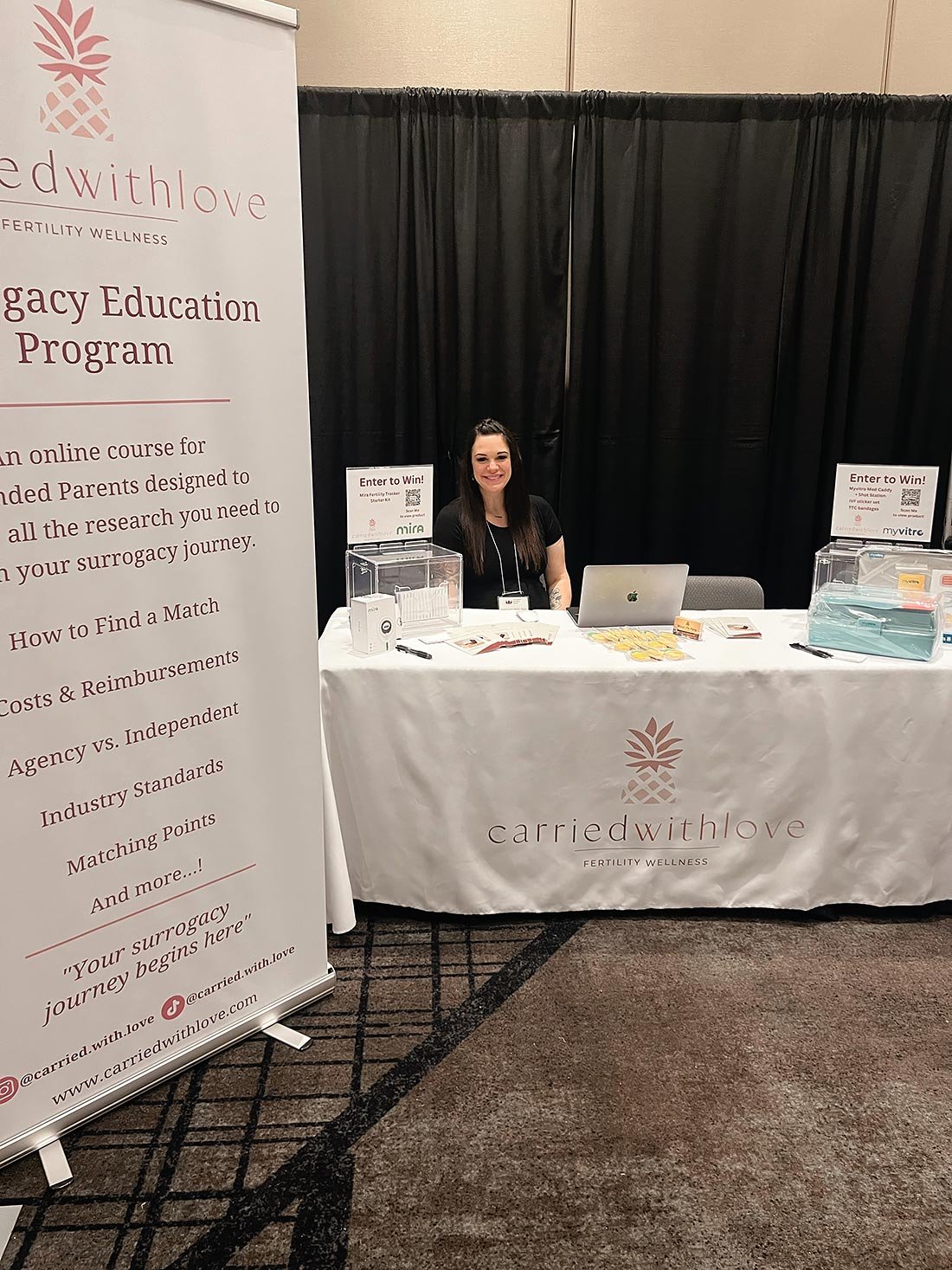 Ariel seated at a booth promoting a surrogacy education program at an event.