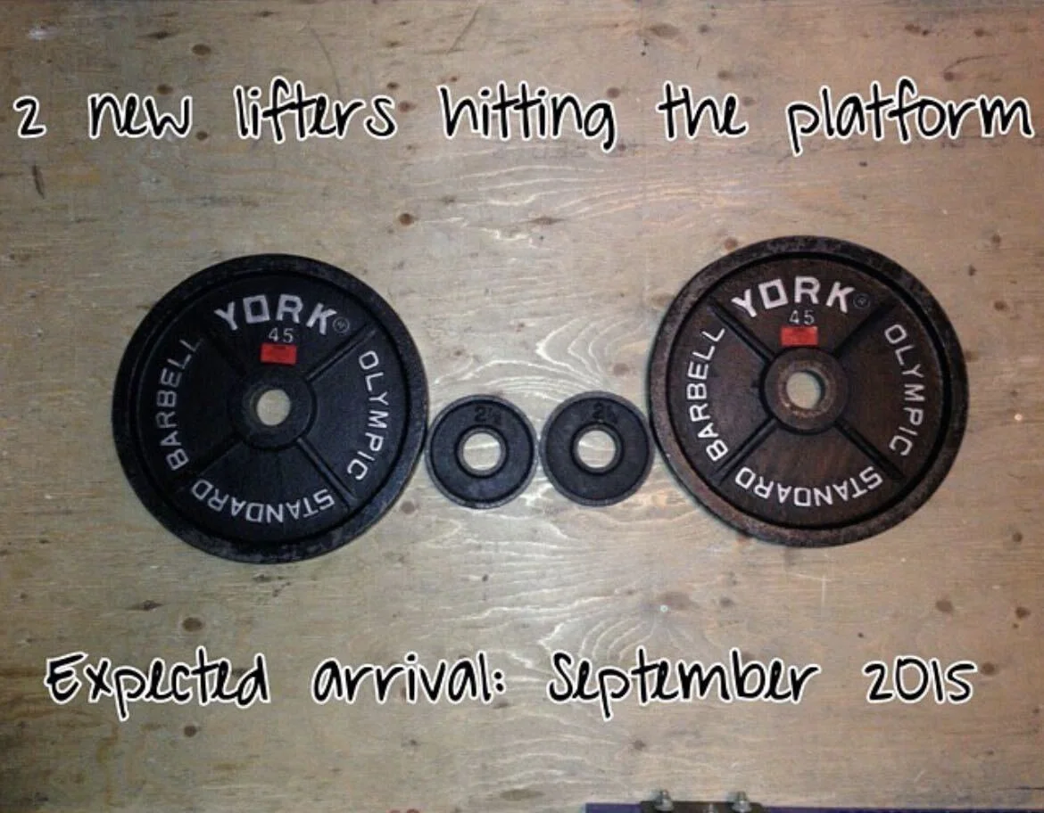 Weightlifting-themed pregnancy announcement with two large barbell plates and two small plates, reading "2 new lifters hitting the platform, expected arrival September 2015"