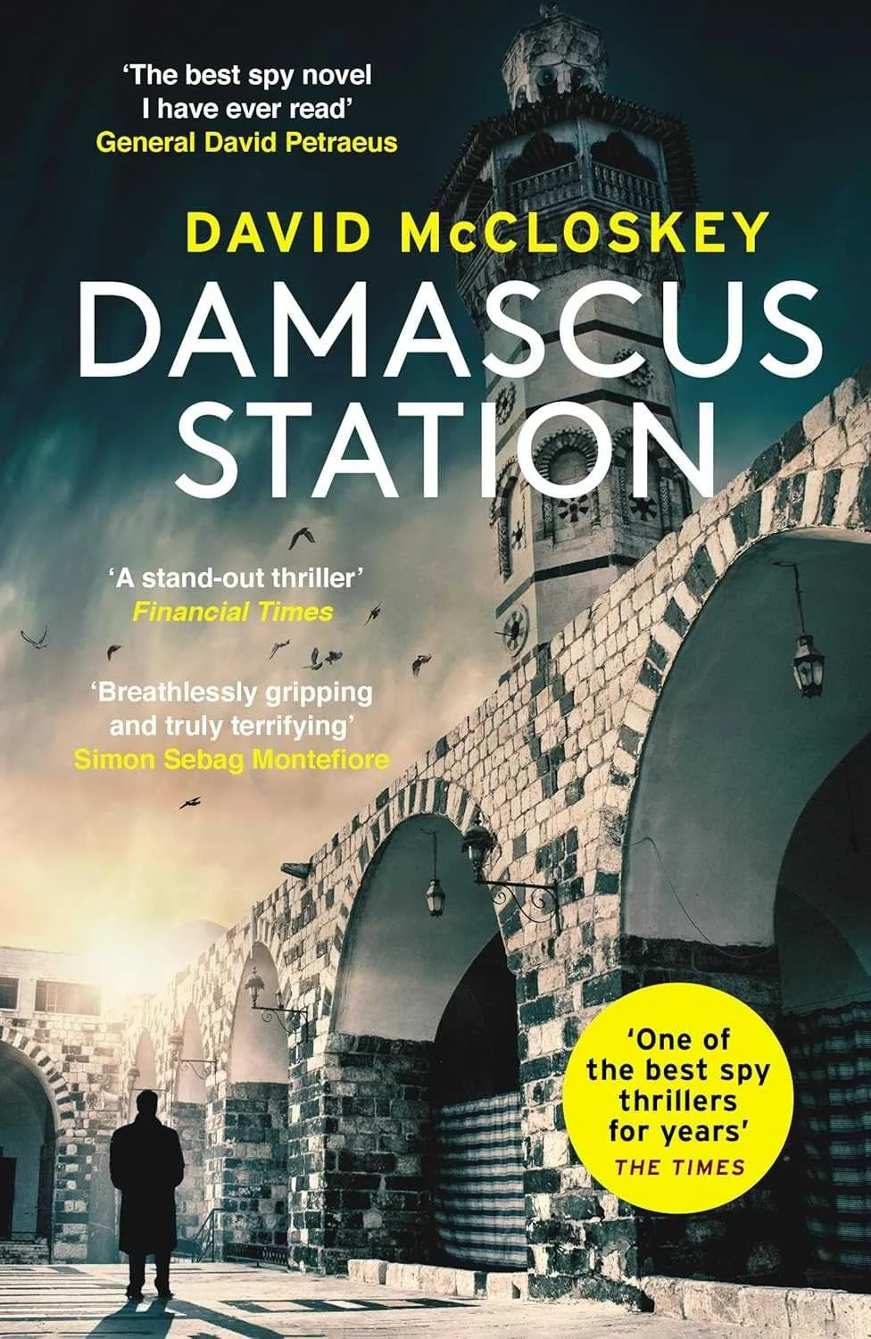 Book cover of 'Damascus Station' by David McCloskey, featuring an image of a historic stone tower and arches in Damascus, with a silhouette of a man walking beneath them, overlaid with quotes from critics.