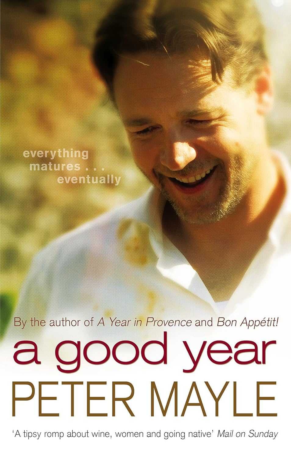 Close-up of a smiling man with light brown hair and a beard, outdoors with blurred natural background, wearing a white shirt.