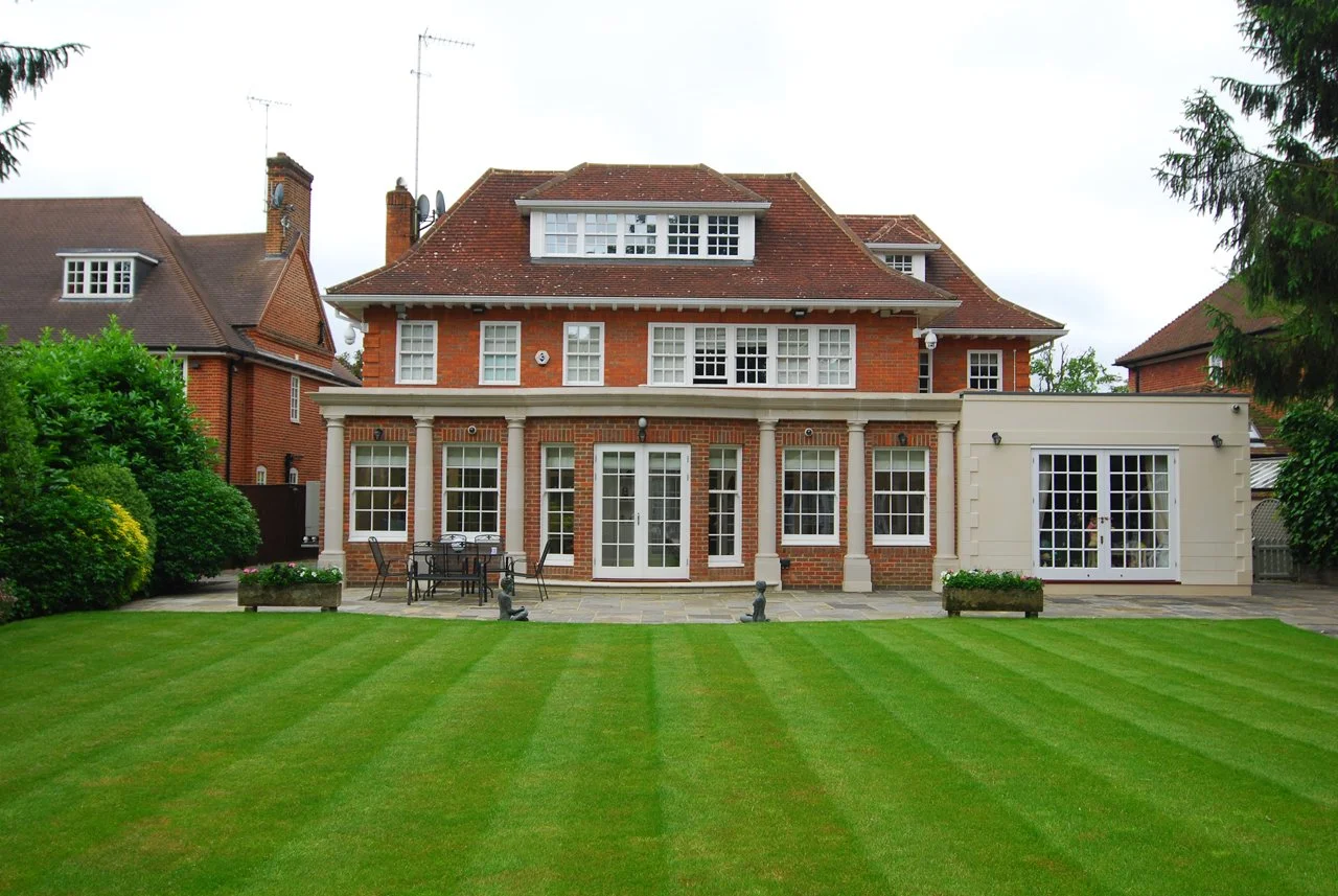 Large red-brick traditional home with tiled roof, white-framed windows, patio, and manicured lawn