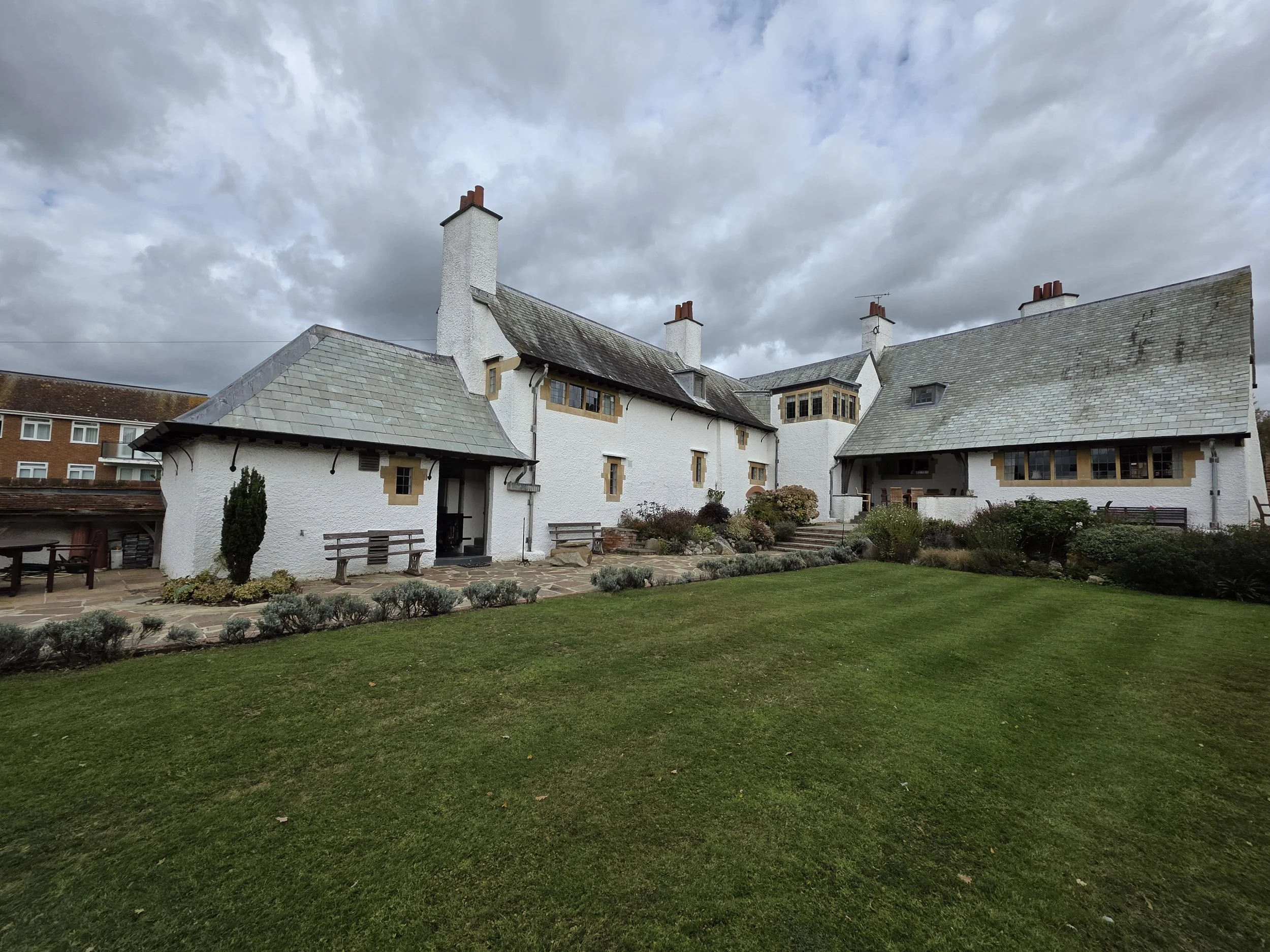 White stucco stone-roofed cottage buildings surrounding a landscaped courtyard under a cloudy sky