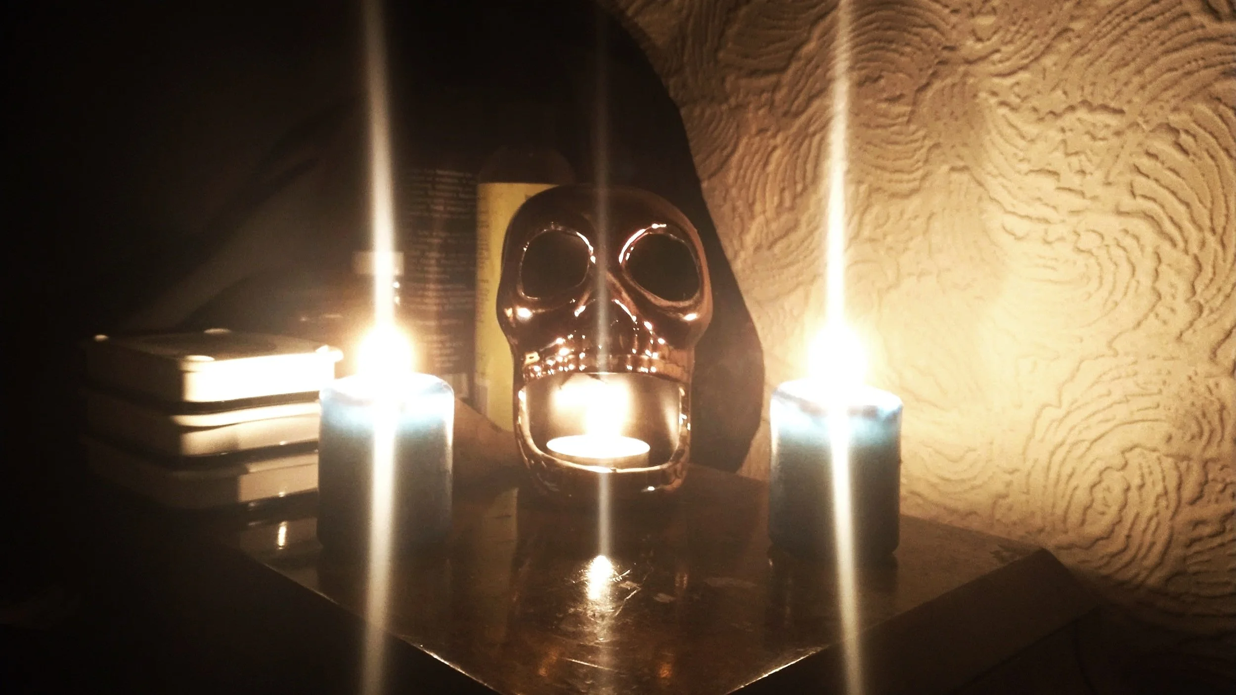 A trio fo candles burnign on an altar, the middle of which sits in a golden skull