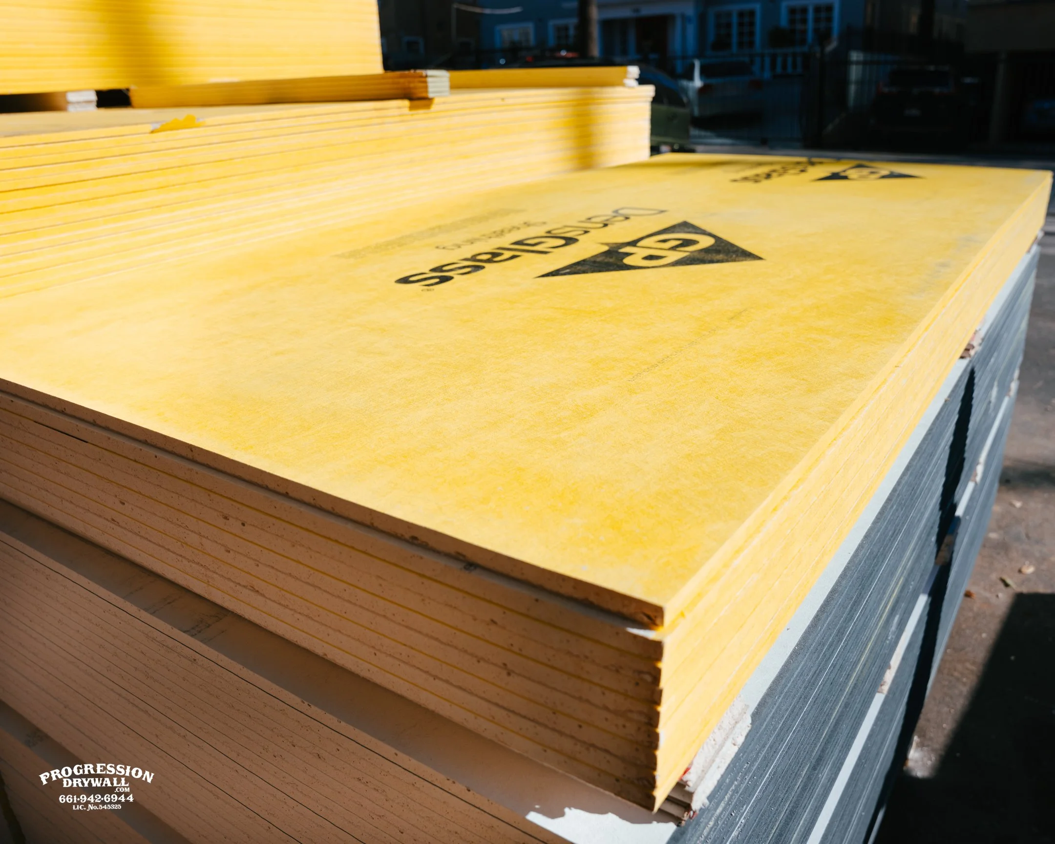 Stack of PABCO dry wall joint compound boxes wrapped with a green strap on a wooden pallet at a construction site.