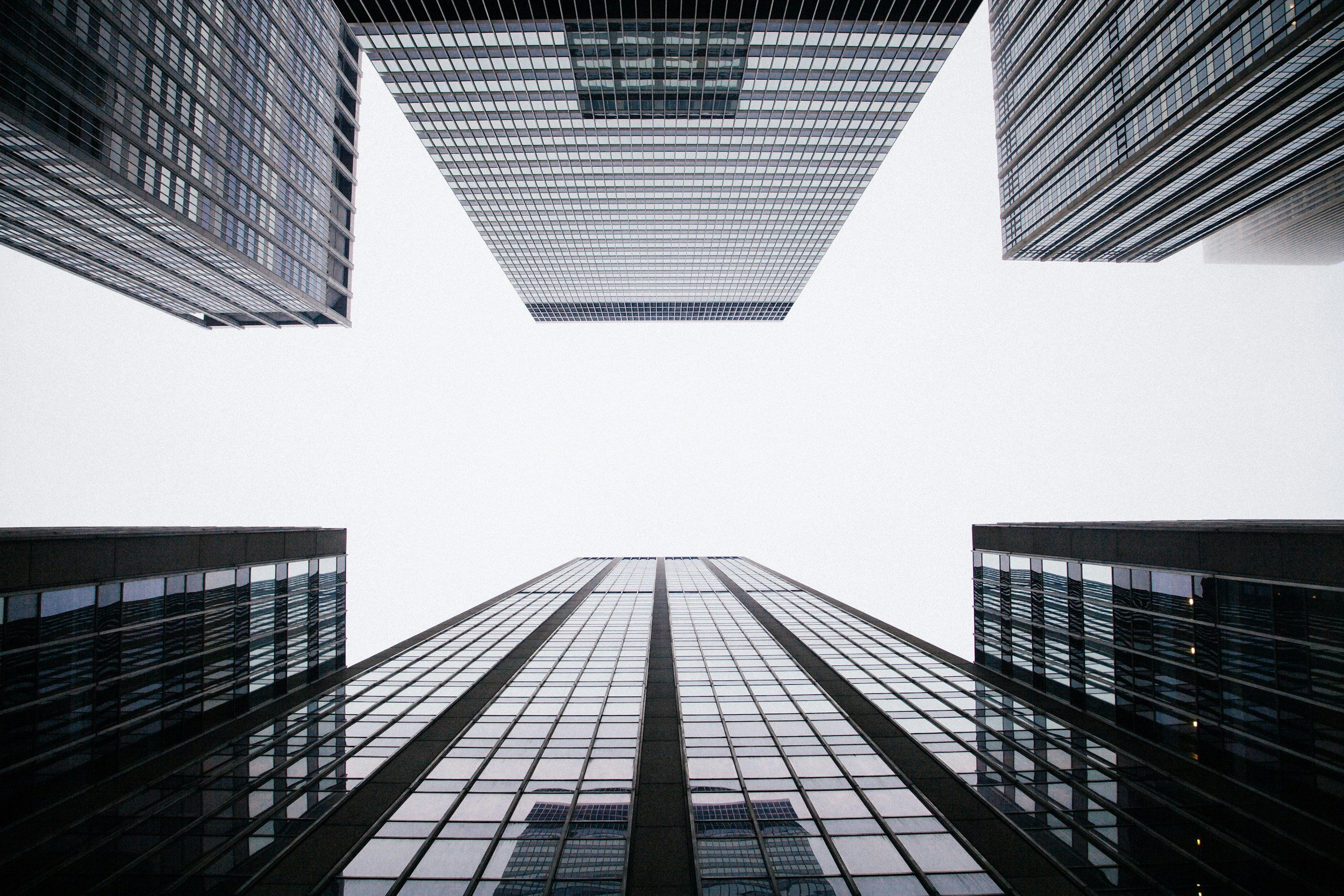 Looking up at four tall glass skyscrapers from ground level, with a cloudy sky overhead.