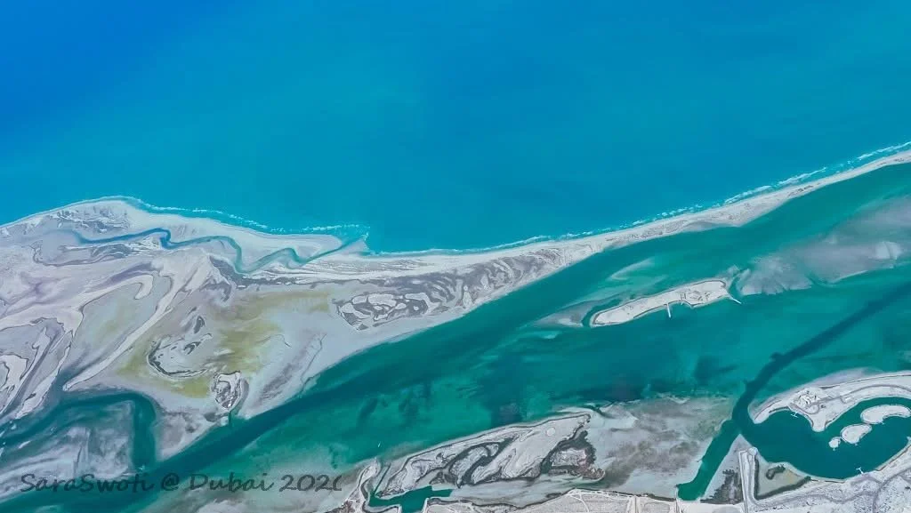 From the plane, somewhere near Dubai: the deep emerald of the ocean weaving itself into the sand. A border not of separation, but of intricate, endless conversation—land and water stitching a new coast below. 