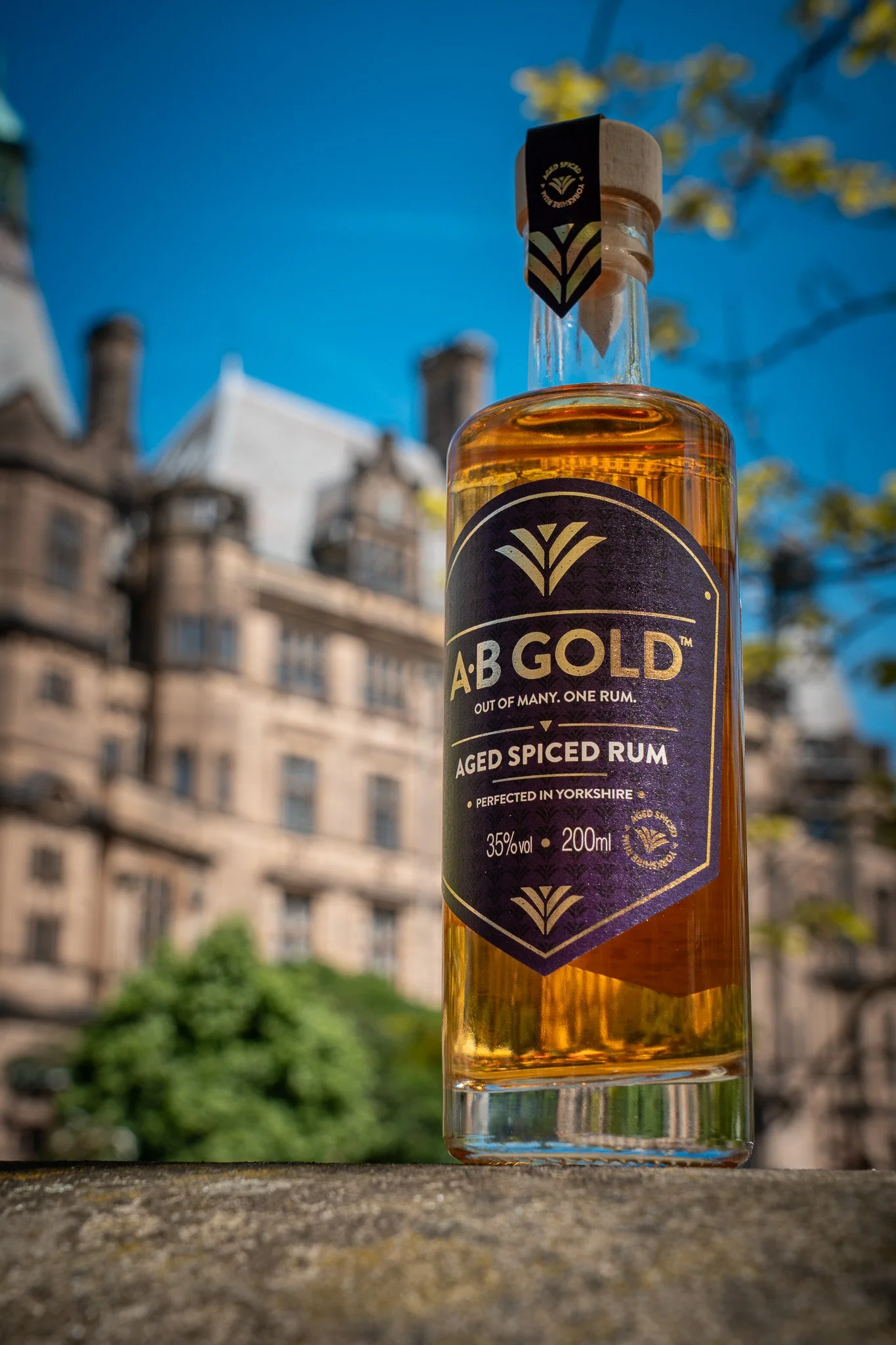 A bottle of AB Gold aged spiced rum outdoors with a cityscape background under a blue sky.