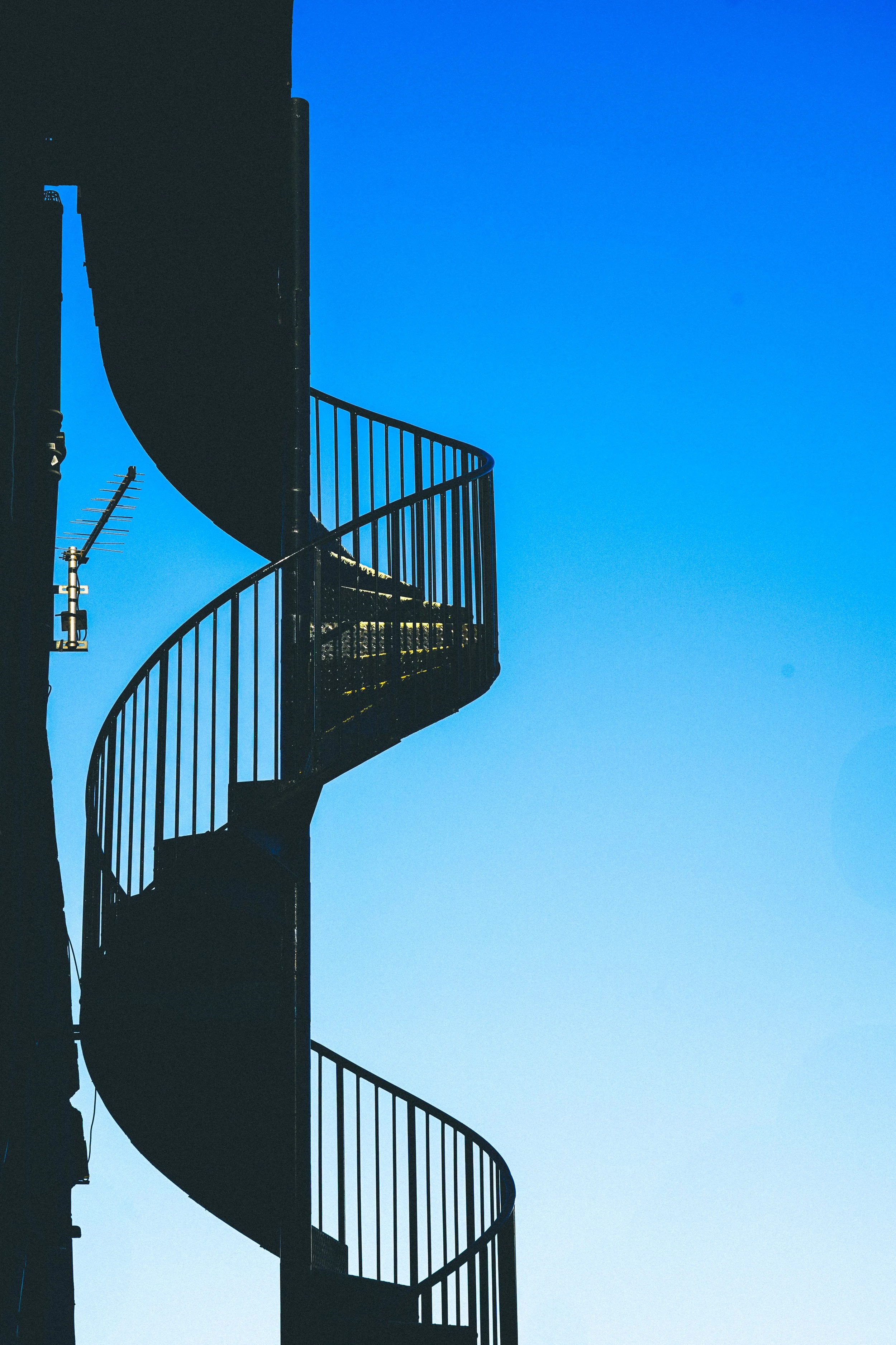A black spiral fire escape with railings against a clear blue sky.