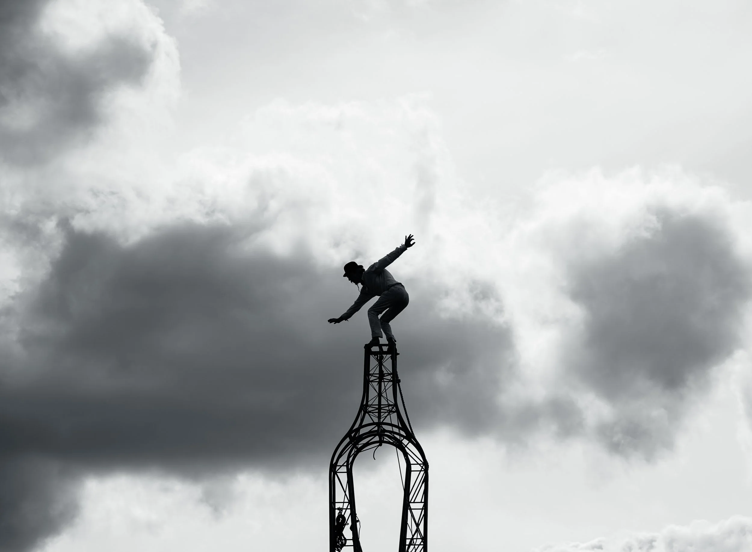 A silhouette of a person balancing on top of a tall metal structure against a cloudy sky.